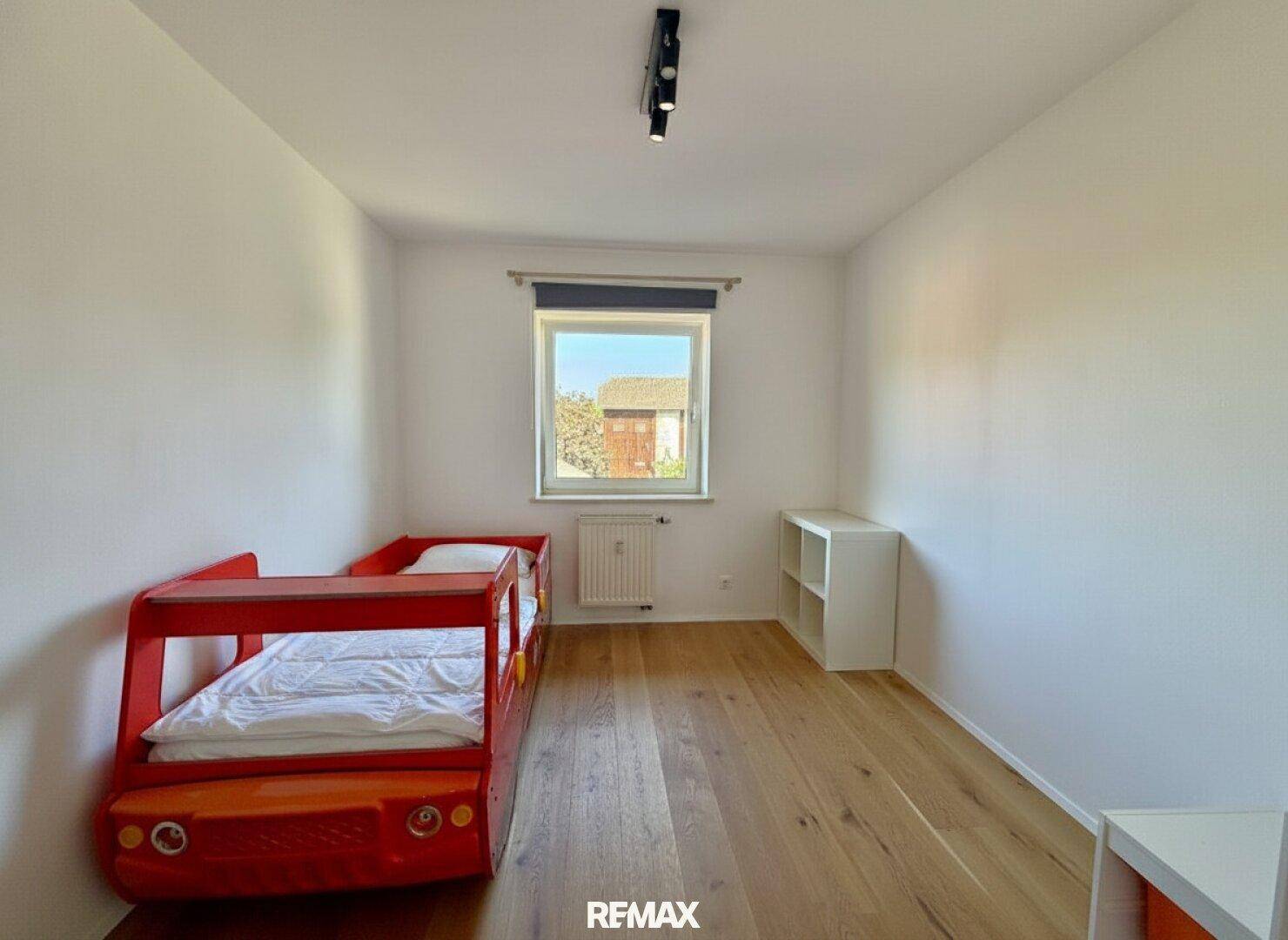 Kinderzimmer mit Holzboden, rotem Autobett und Fenster für Tageslicht.
