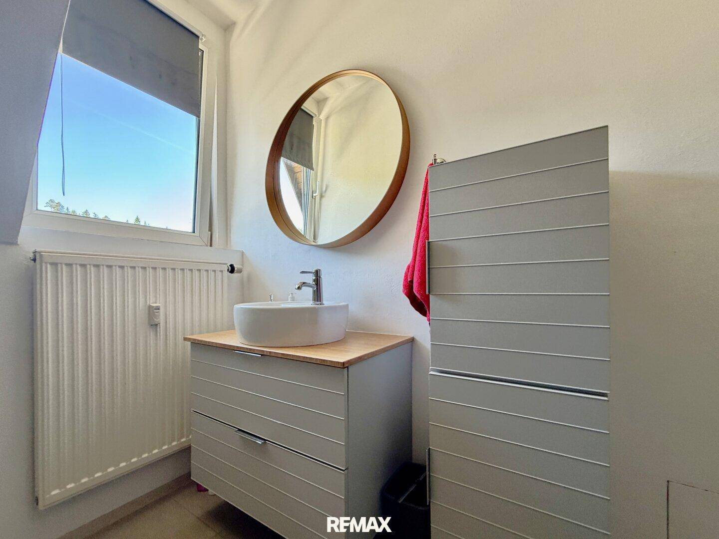 Modernes Badezimmer mit Aufsatzwaschbecken, rundem Spiegel und Fenster.