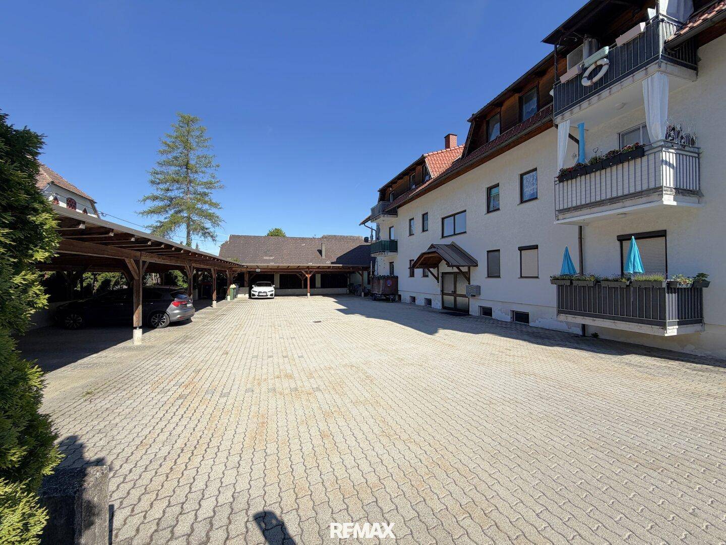 Außenansicht des Gebäudes mit großem gepflasterten Parkplatz und Carports.