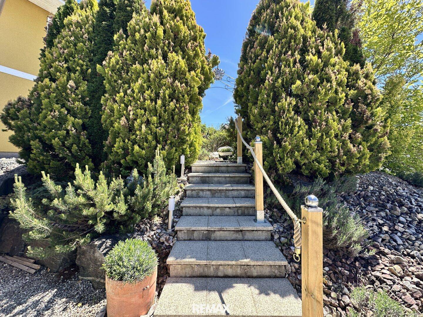 Steintreppe im Außenbereich, umgeben von üppiger Bepflanzung und Felsen im Garten.