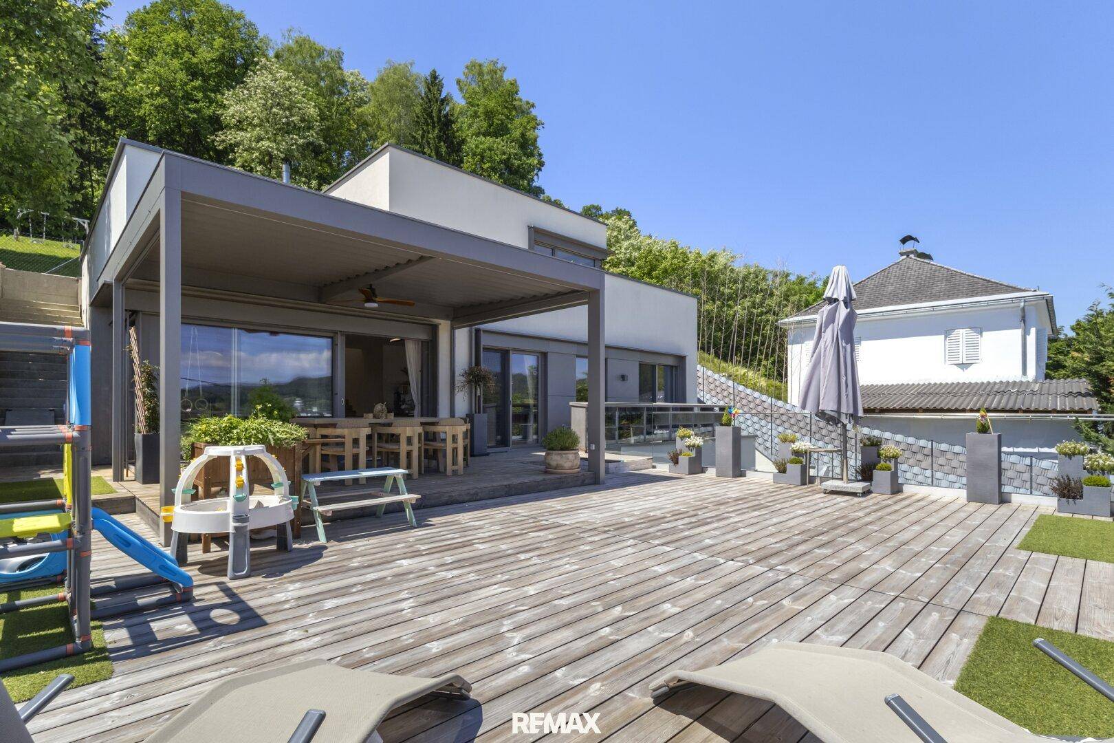 Große Holzterrasse mit überdachtem Essbereich und Liegestühlen, ideal zum Entspannen.
