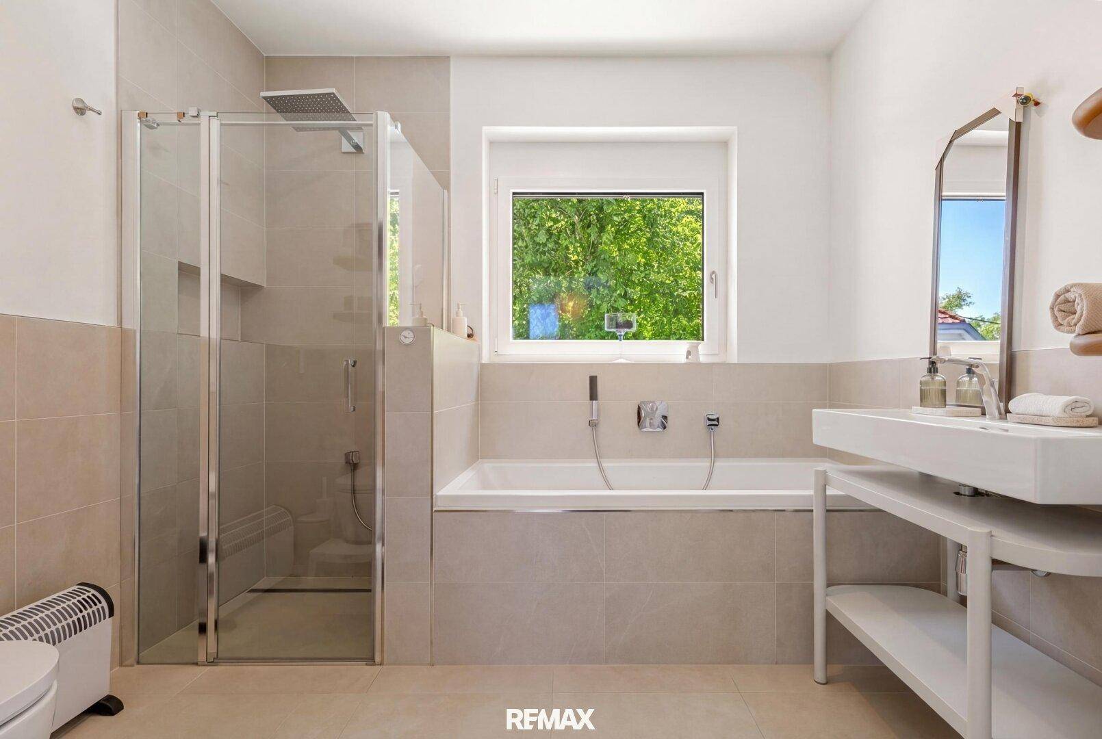 Modernes Badezimmer mit Dusche, Badewanne und Fenster für natürliches Licht.
