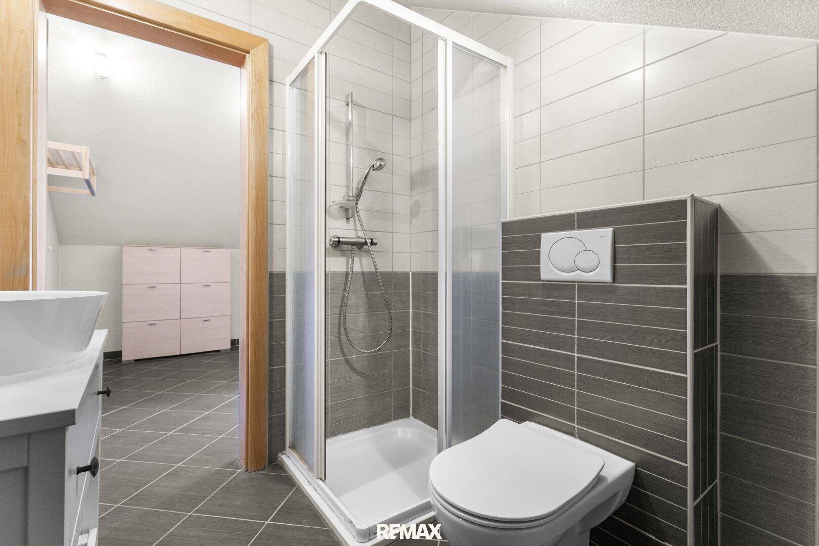Modernes Badezimmer im Dachgeschoss mit Dusche, WC und grauen Fliesen.