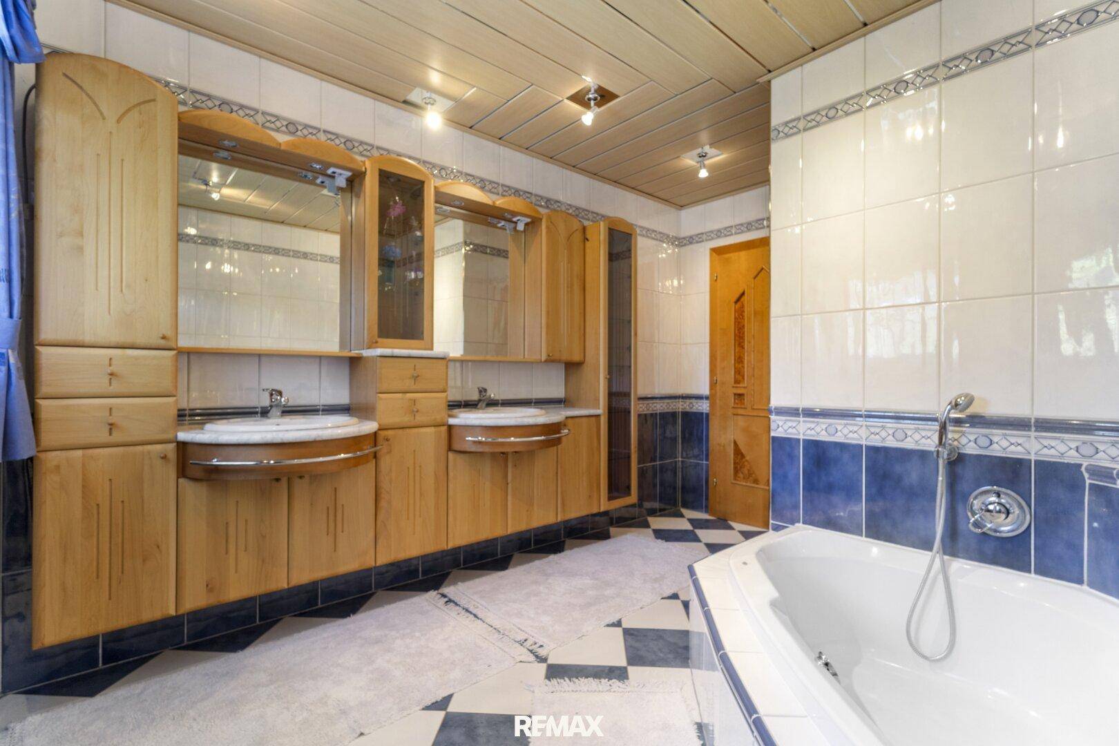 Geräumiges Badezimmer mit Doppelwaschbecken, Eckbadewanne und blauen Fliesen.