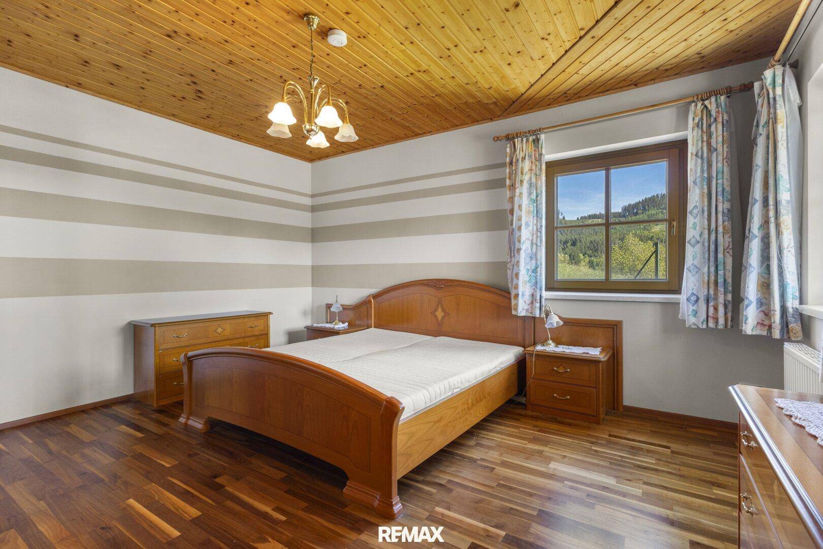 Schlafzimmer mit Holzboden, Holzbalkendecke und traditionellen Möbeln.