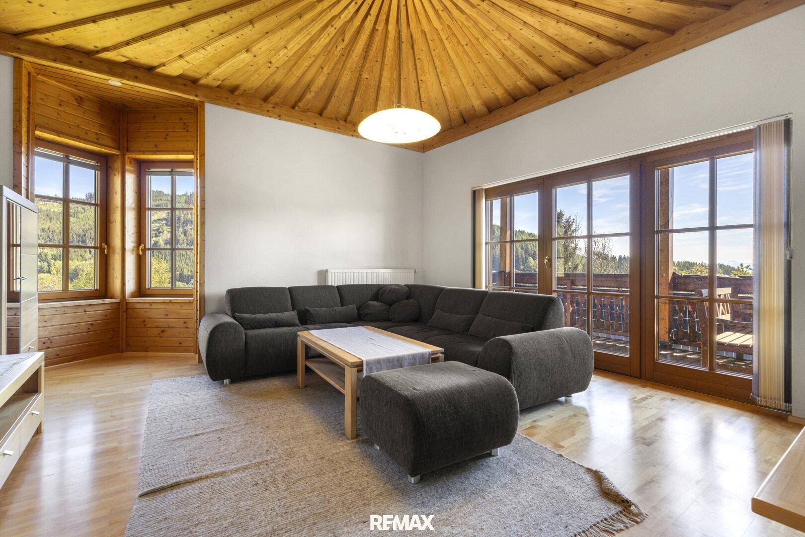 Gemütliches Wohnzimmer mit großem Sofa, Holzbalkendecke und Zugang zum Balkon.