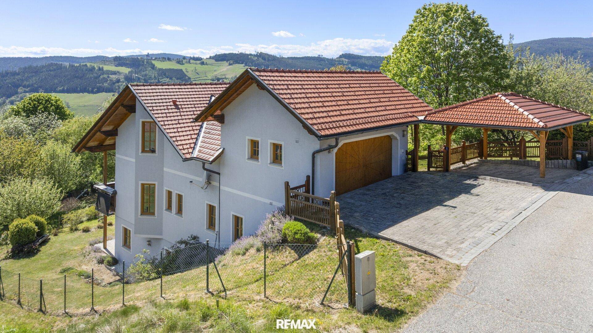 Seitenansicht des Hauses mit Garage, Carport und Blick auf die umliegende Hügellandschaft.