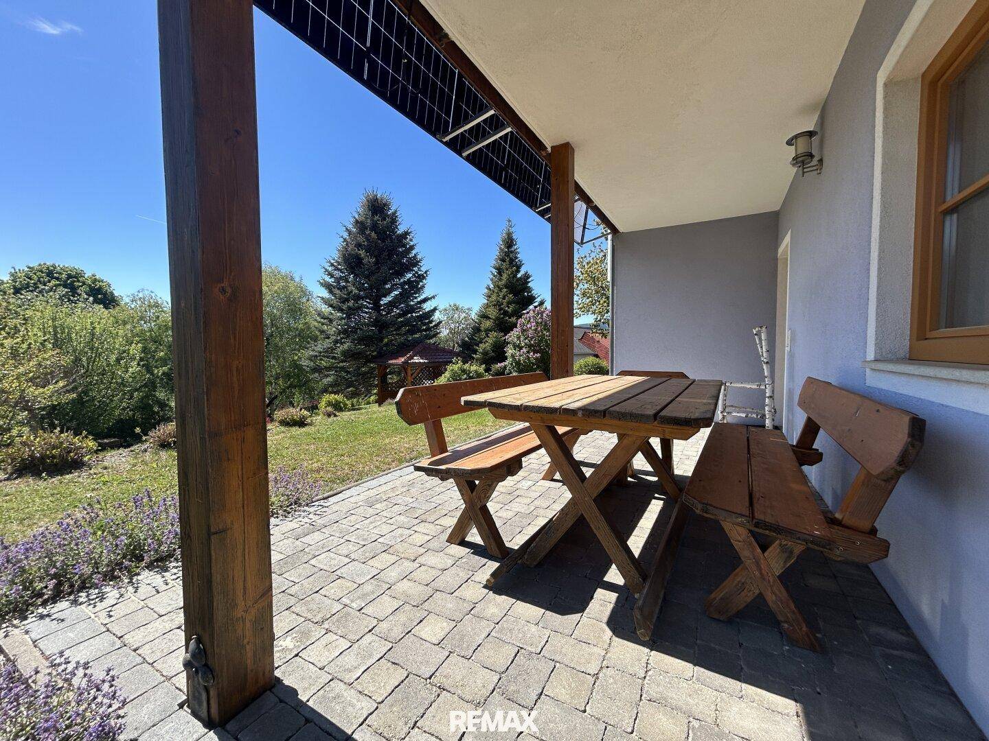 Gemütliche überdachte Terrasse mit Holzbänken und Blick auf den Garten.