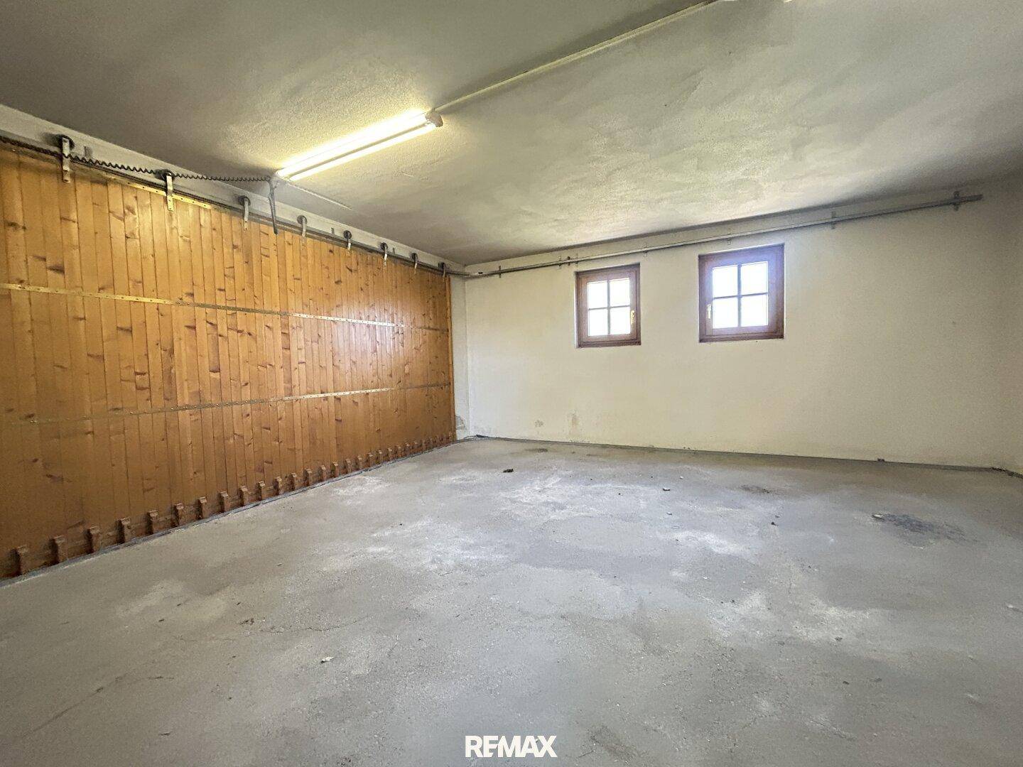 Geräumige Garage mit Holzwandverkleidung und zwei kleinen Fenstern, ideal als Abstellraum.