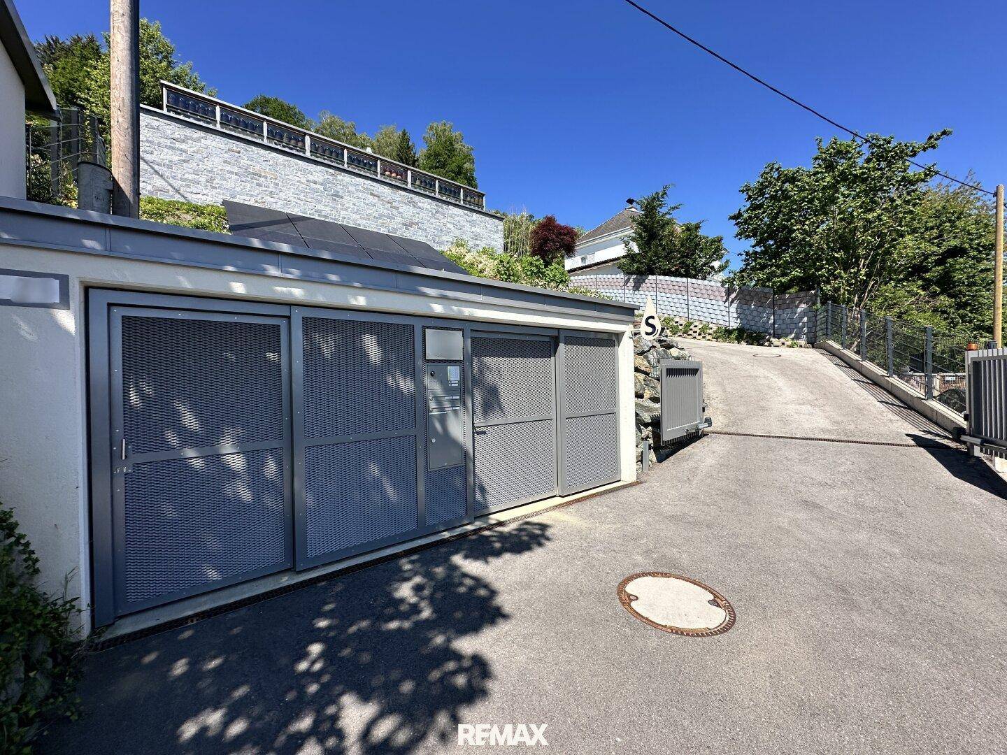 Garageneinfahrt mit modernen Metalltoren und einer Zufahrt zur Immobilie auf einem Hanggrundstück.