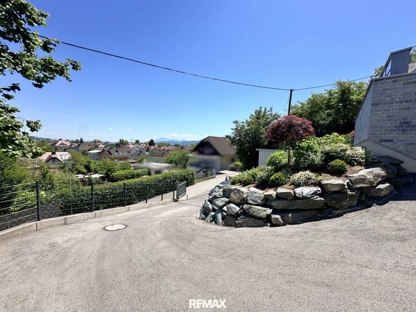 Weitläufige Auffahrt mit gepflegter Bepflanzung, Felsen und einem Panoramablick in die Umgebung.