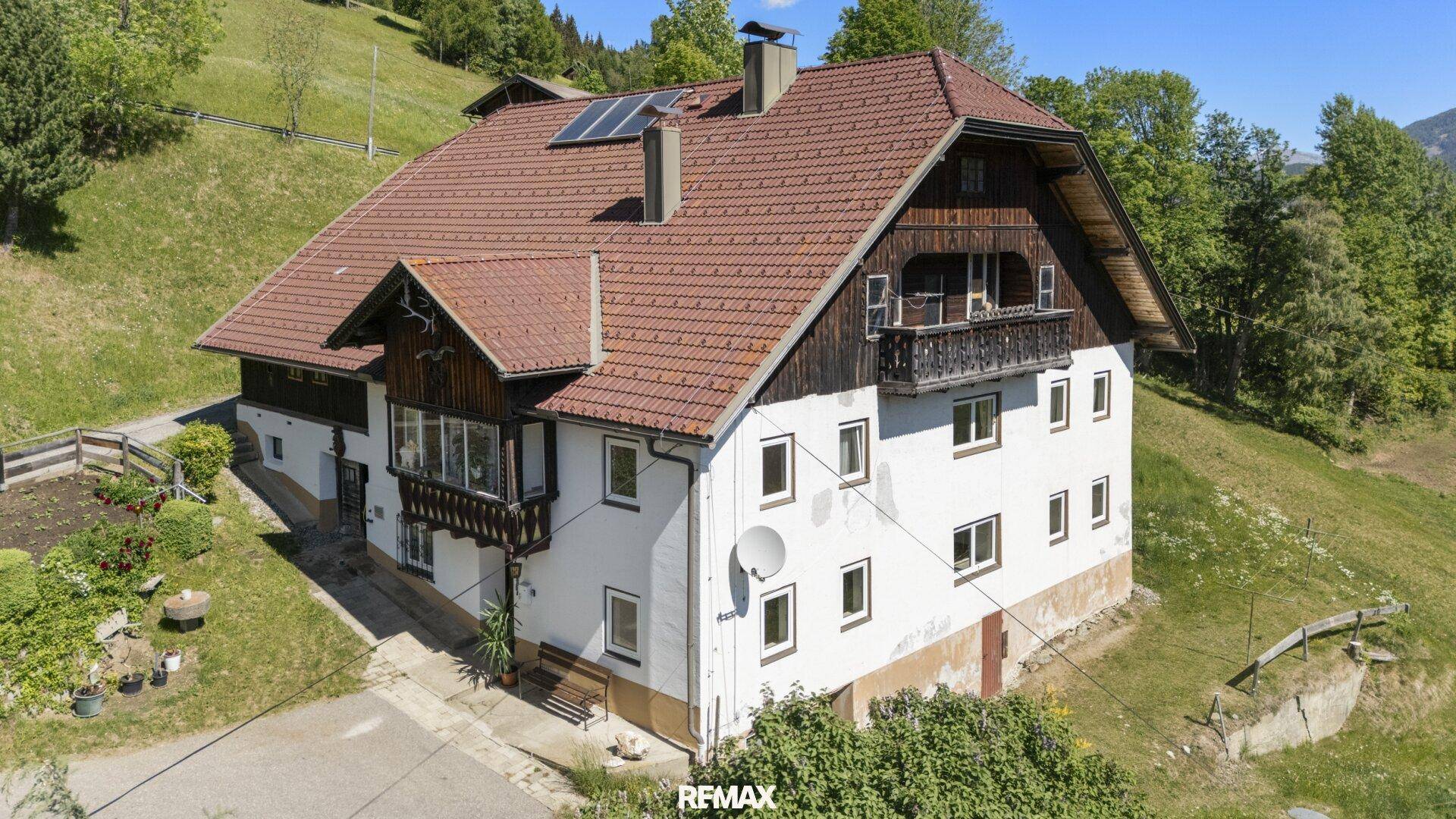 Traditionelles Wohnhaus mit rotem Ziegeldach, weißer Fassade und Holzbalkonen, umgeben von grünen Hängen.