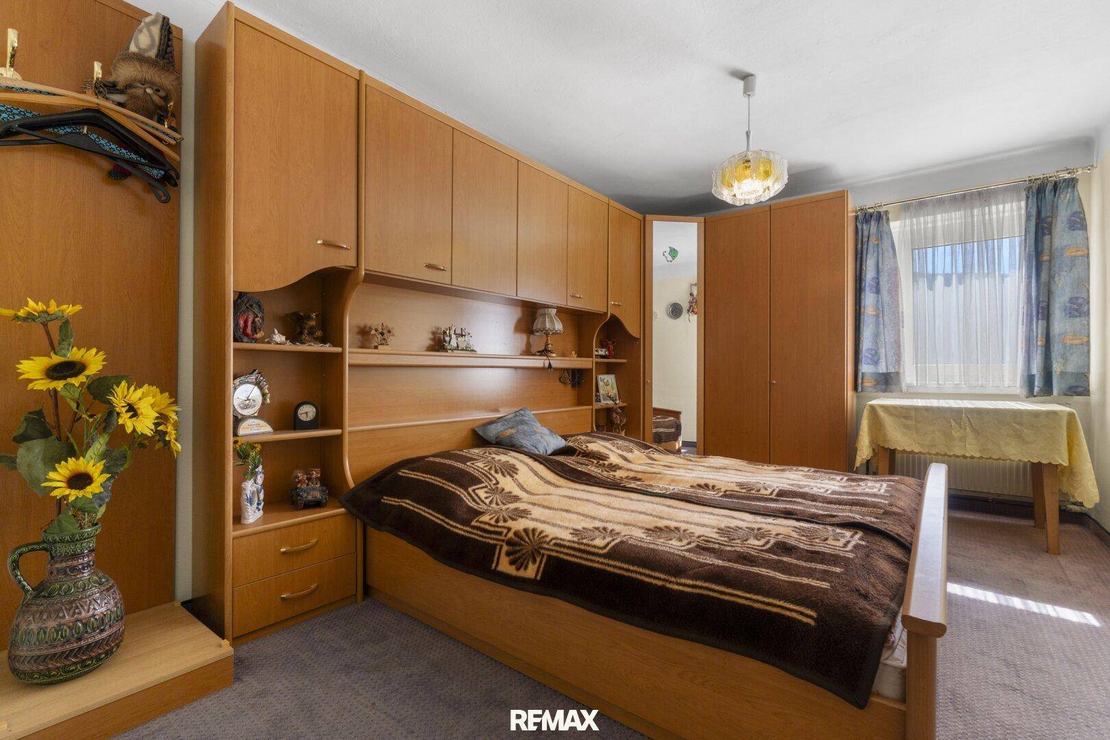 Schlafzimmer mit großem, eingebautem Holzschrank und Bettrahmen, Fenster mit Vorhängen und Teppichboden.