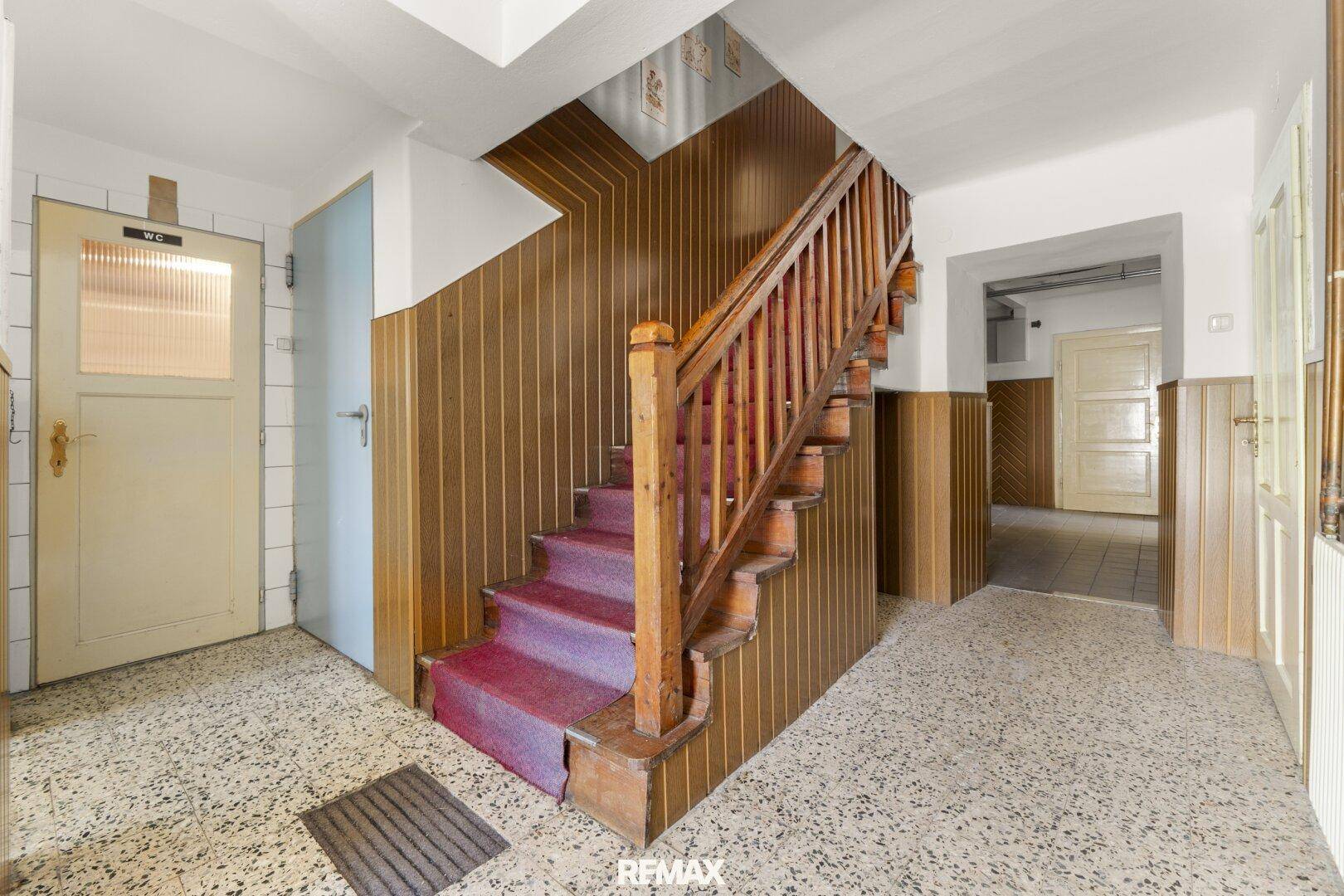 Altertümlicher Eingangsbereich mit Holztreppe, gemusterten Fliesen und Holzvertäfelung an den Wänden.