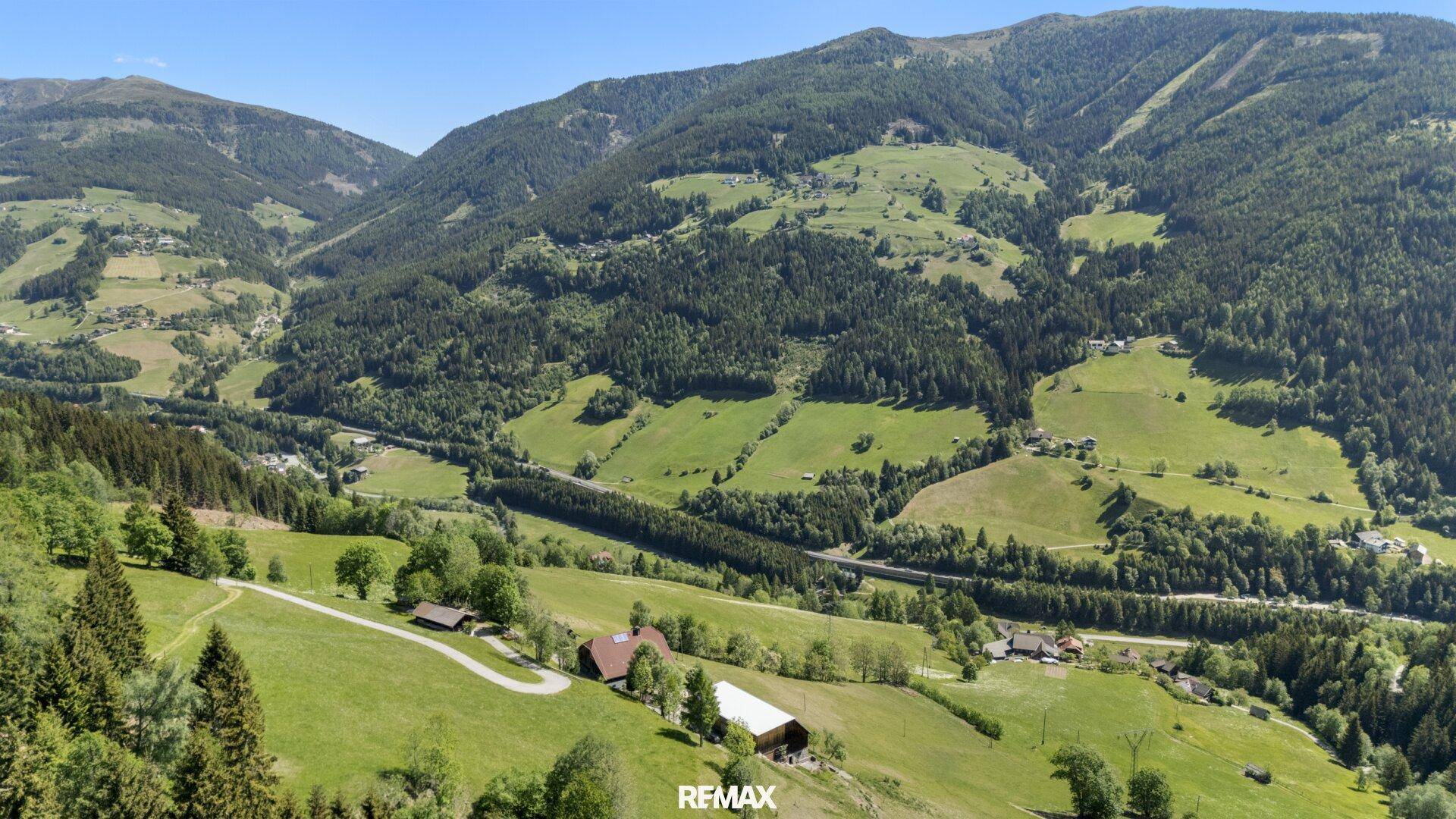 Weitwinkel-Luftaufnahme des Tals, die das Anwesen mit Haus und Scheune in der Landschaft zeigt.