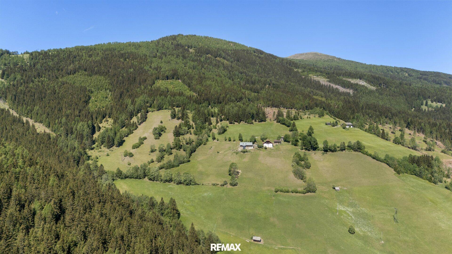 Weitläufige Luftaufnahme des Berggebiets mit dichten Wäldern und ausgedehnten grünen Wiesen.
