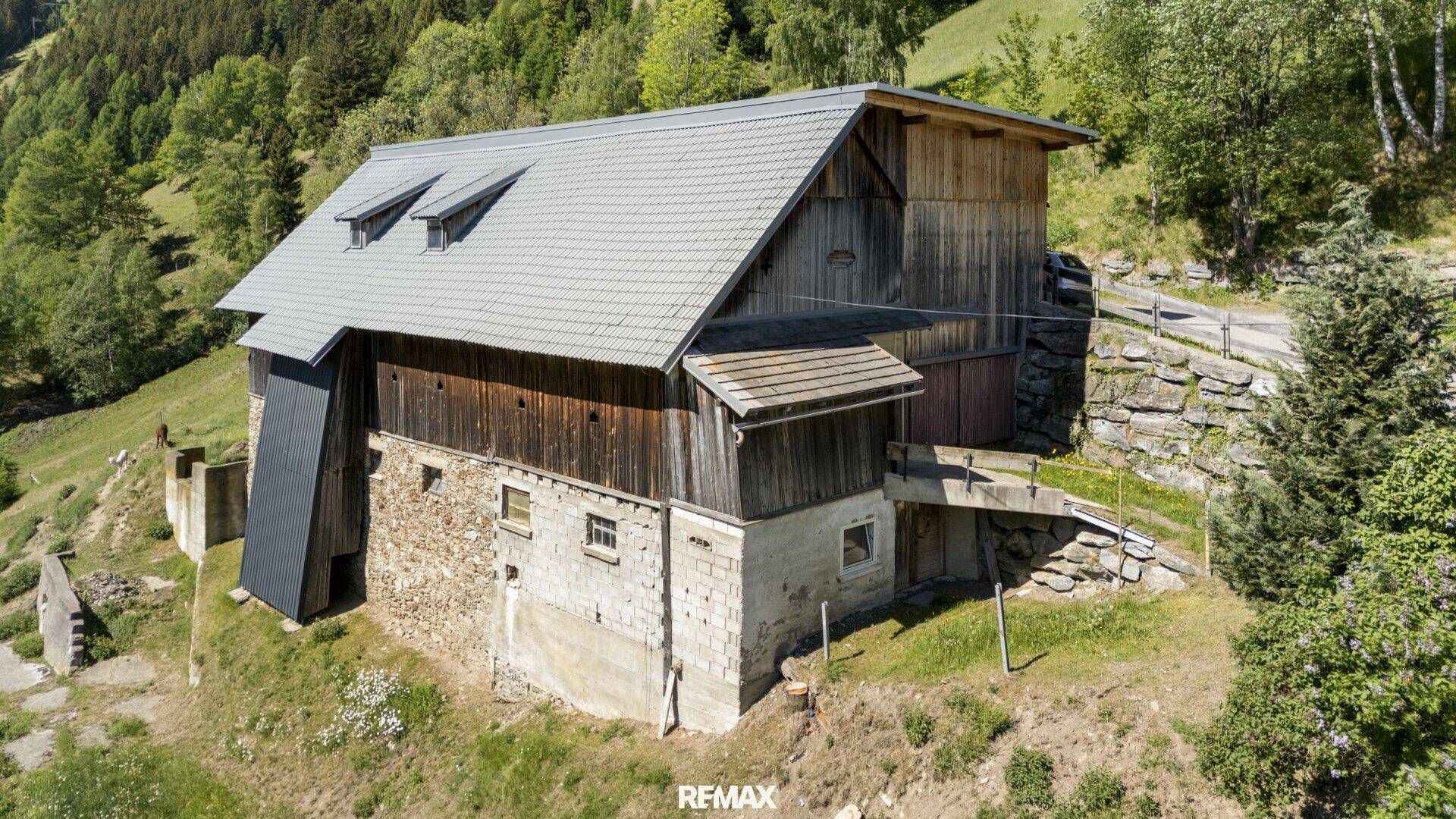 Luftaufnahme des Scheunengebäudes, das seine Stein- und Holzkonstruktion sowie das graue Dach zeigt.