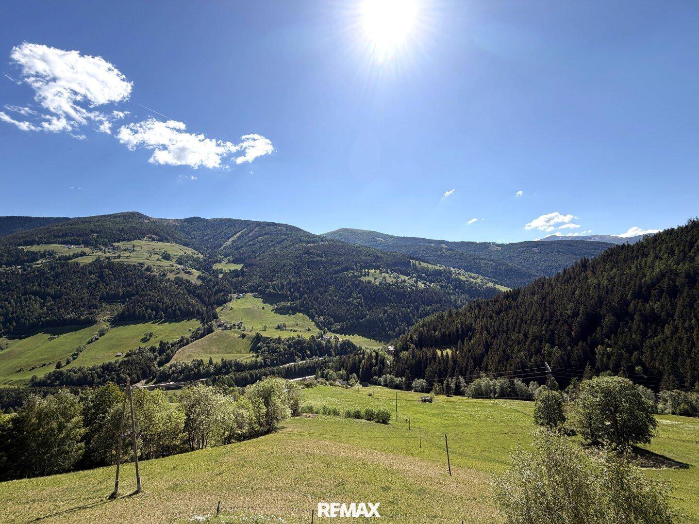 Weitläufige Berglandschaft mit grünen Wiesen und dichten Wäldern unter strahlend blauem Himmel und Sonnenschein.