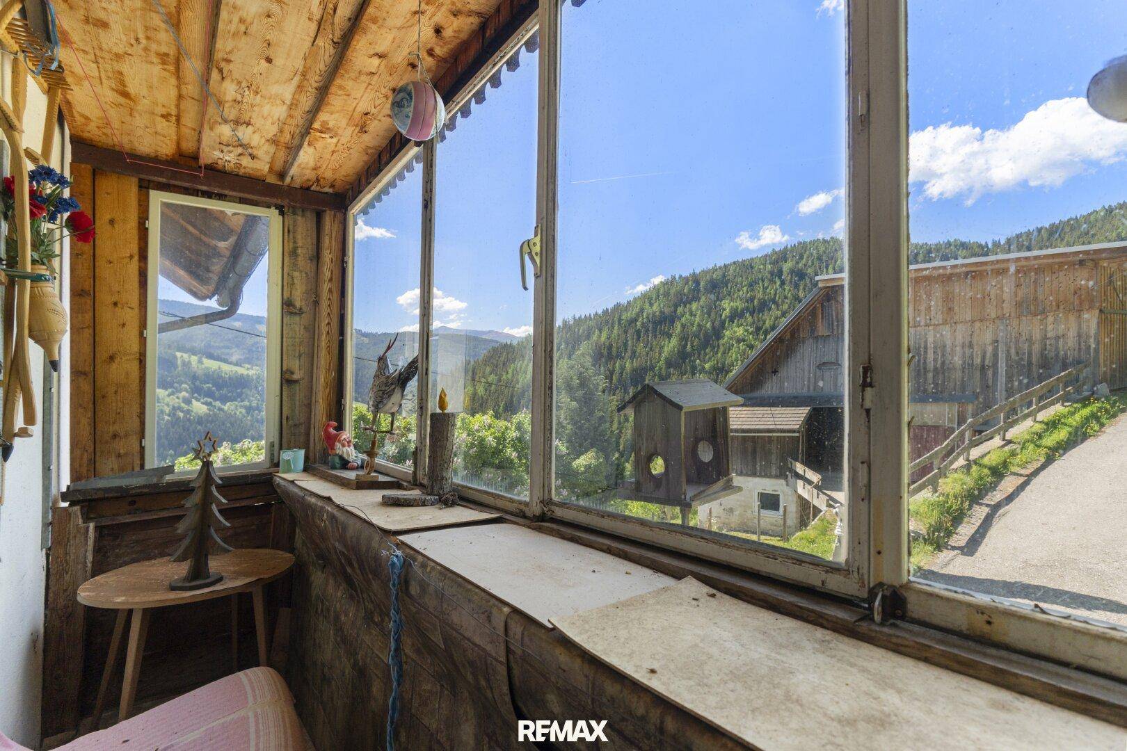 Verglaster Balkon oder Wintergarten mit Holzwänden und -decke, bietet weiten Blick auf die Landschaft und Nachbargebäude.