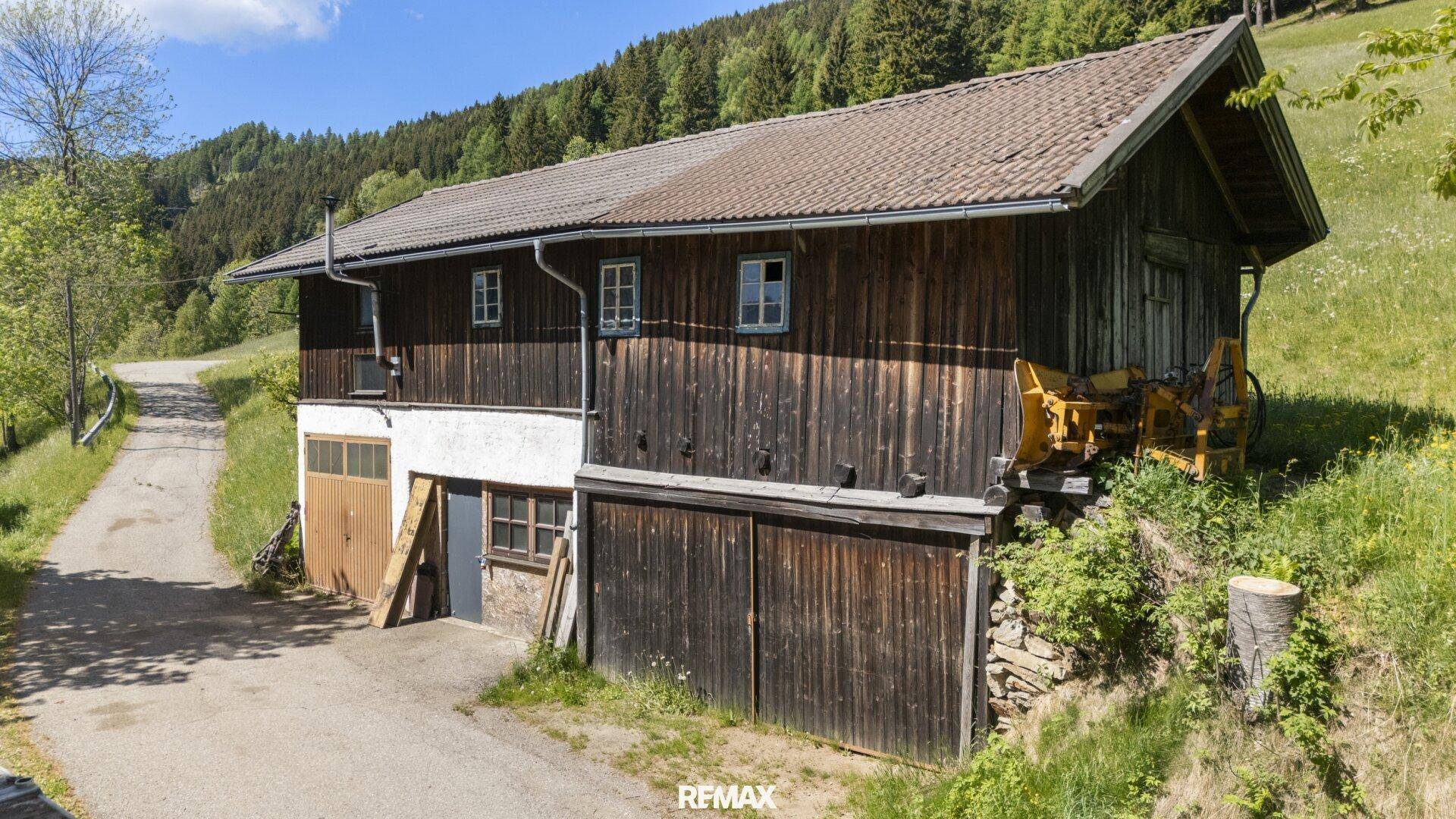 Außenansicht eines weiteren traditionellen Holzgebäudes, möglicherweise eine Scheune oder ein Nebengebäude, mit Zufahrt.