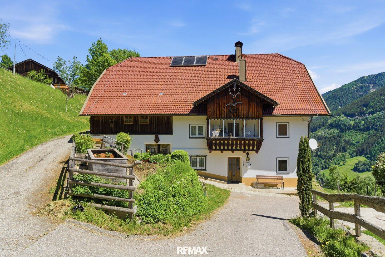 Ansicht des traditionellen Wohnhauses mit Eingangsbereich, Holzbalkonen und Solarpaneelen auf dem Dach.