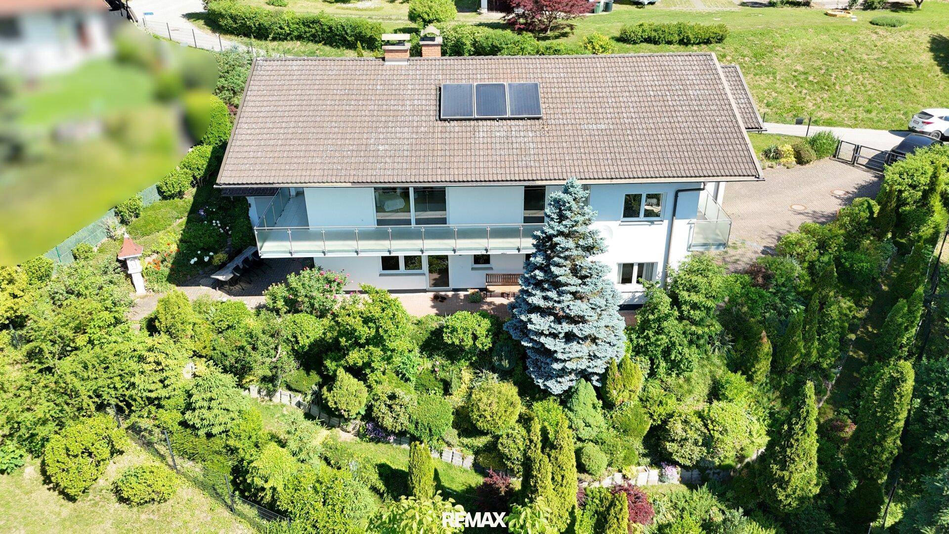Luftaufnahme des Hauses mit gepflegtem Garten und Solarpaneelen auf dem Dach unter blauem Himmel.