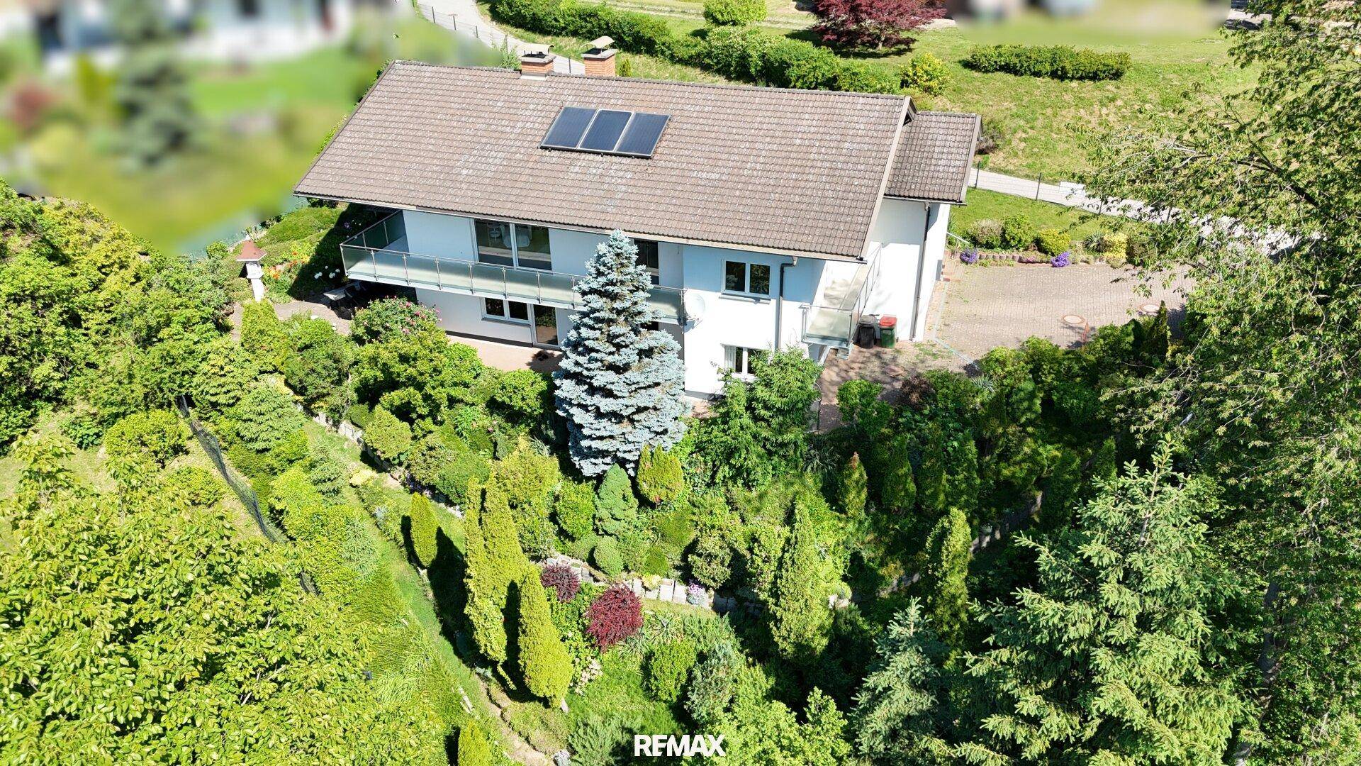 Vogelperspektive des Hauses, eingebettet in eine grüne Landschaft mit vielen Bäumen und Sträuchern.