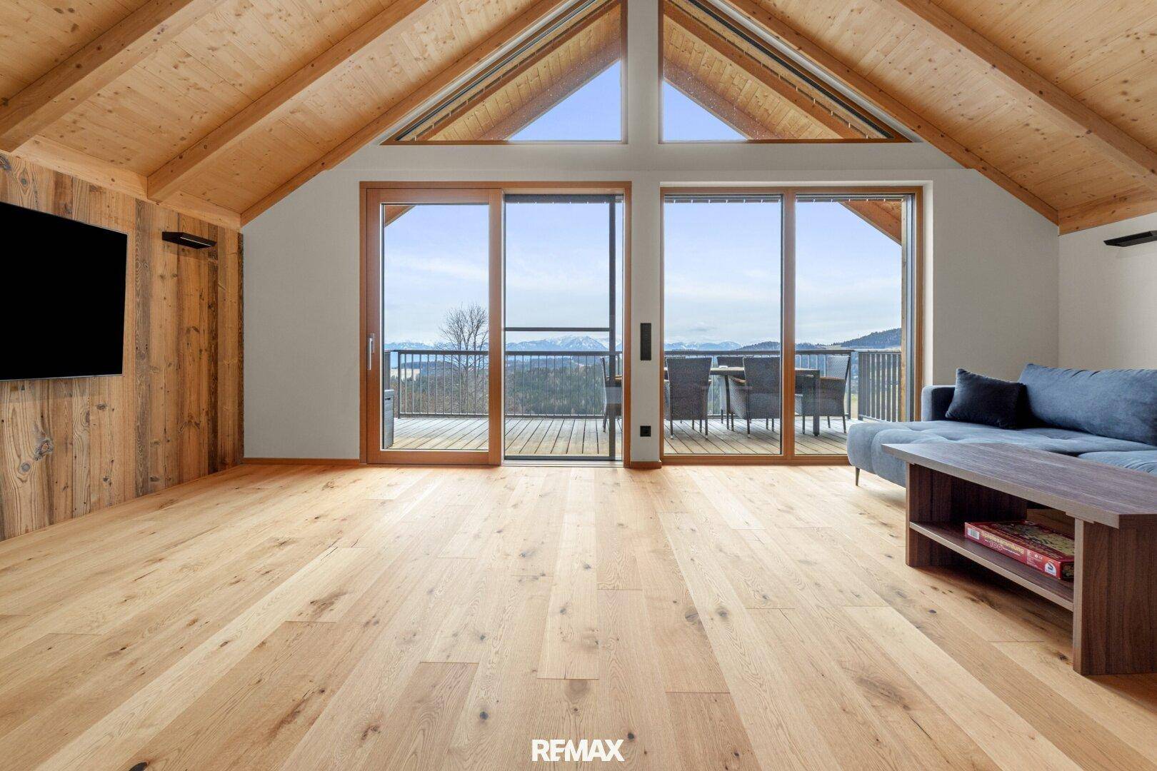 Helles Wohnzimmer mit Holzboden, hohen Decken und Zugang zu einem Balkon mit Bergblick.