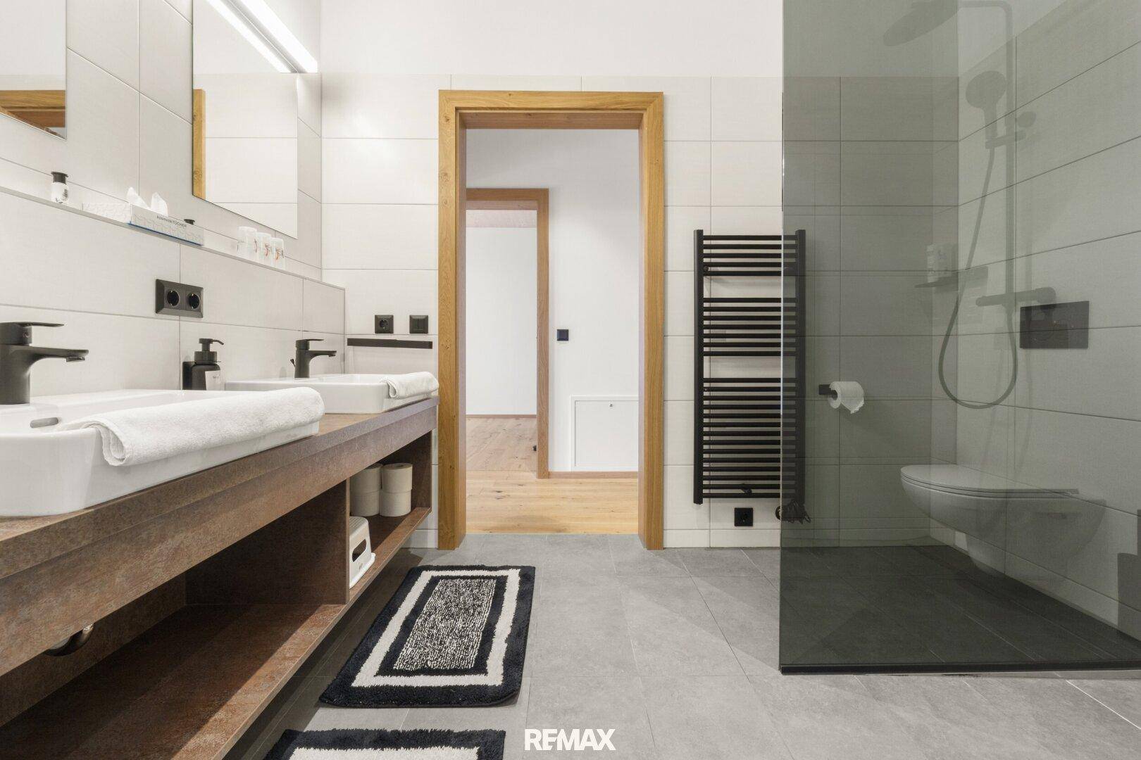 Modernes Badezimmer mit Doppelwaschbecken, begehbarer Dusche und beheiztem Handtuchhalter.