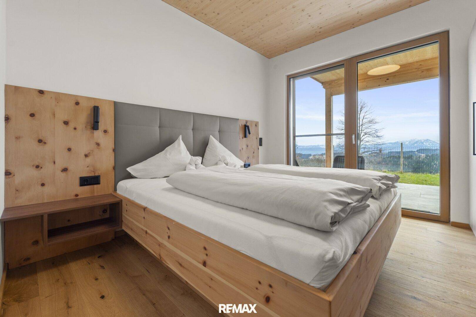 Komfortables Schlafzimmer mit Holzbett, Holzboden und großem Fenster mit Zugang zur Terrasse und Bergblick.