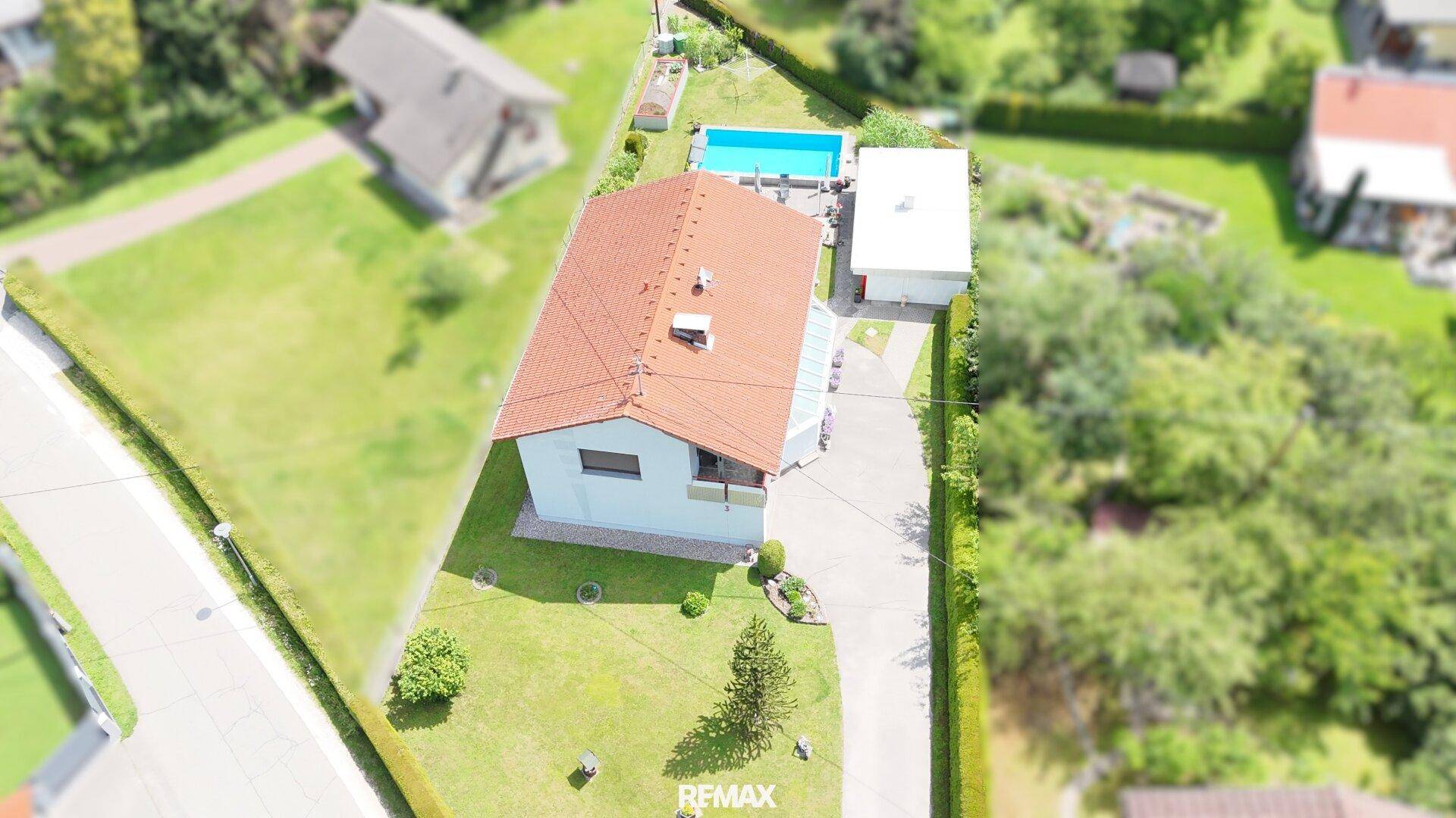 Dachaufsicht des Einfamilienhauses mit Zufahrt und umgebender Grünfläche.