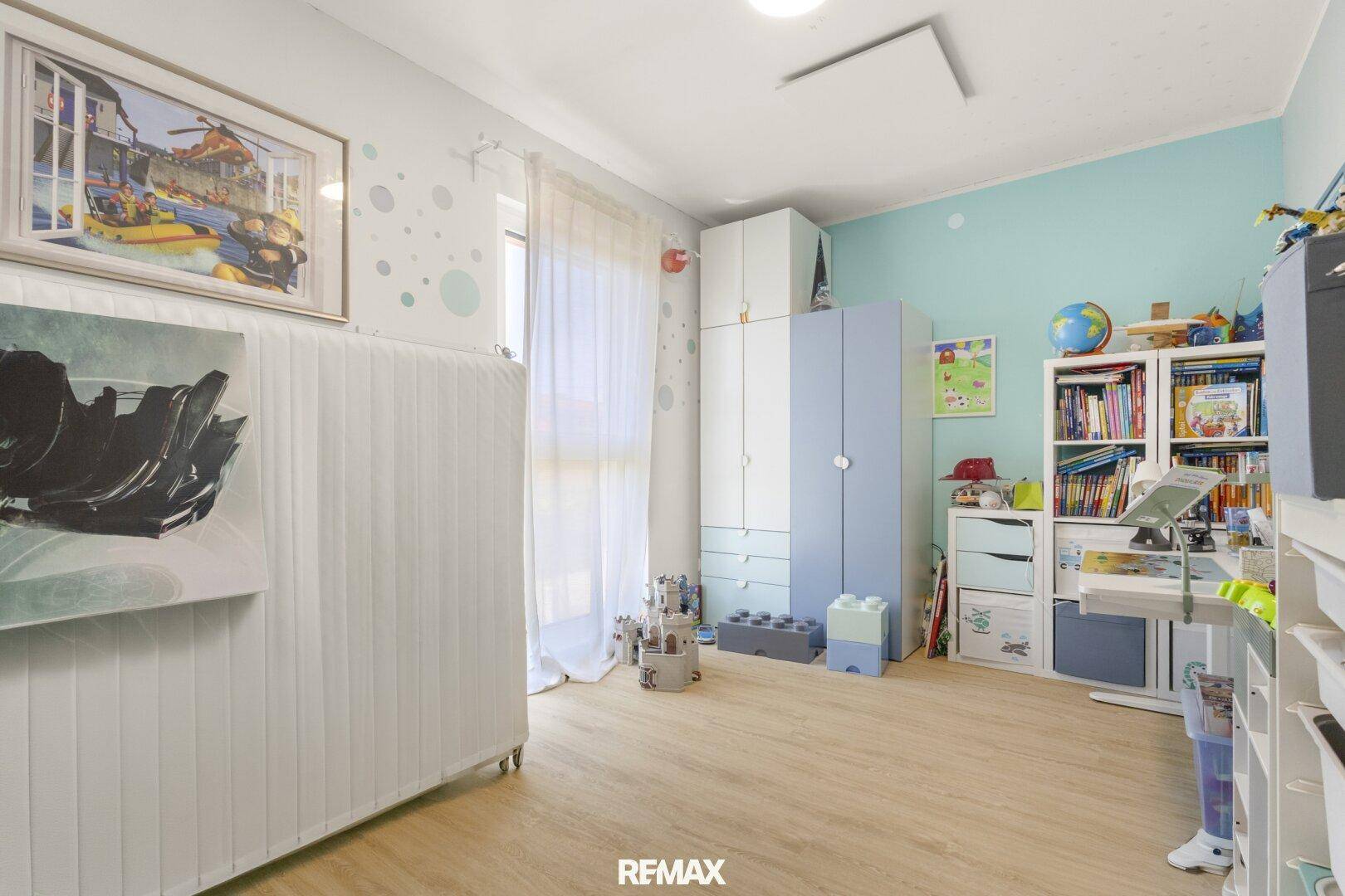 Kinderzimmer mit hellem Laminatboden, bunten Möbeln und viel Stauraum.