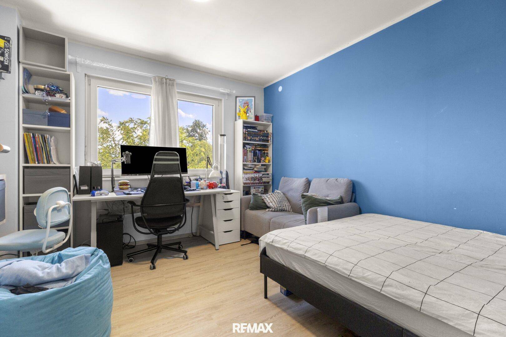 Jugendzimmer mit Schreibtisch, Bett und blauer Akzentwand, ideal zum Lernen und Entspannen.