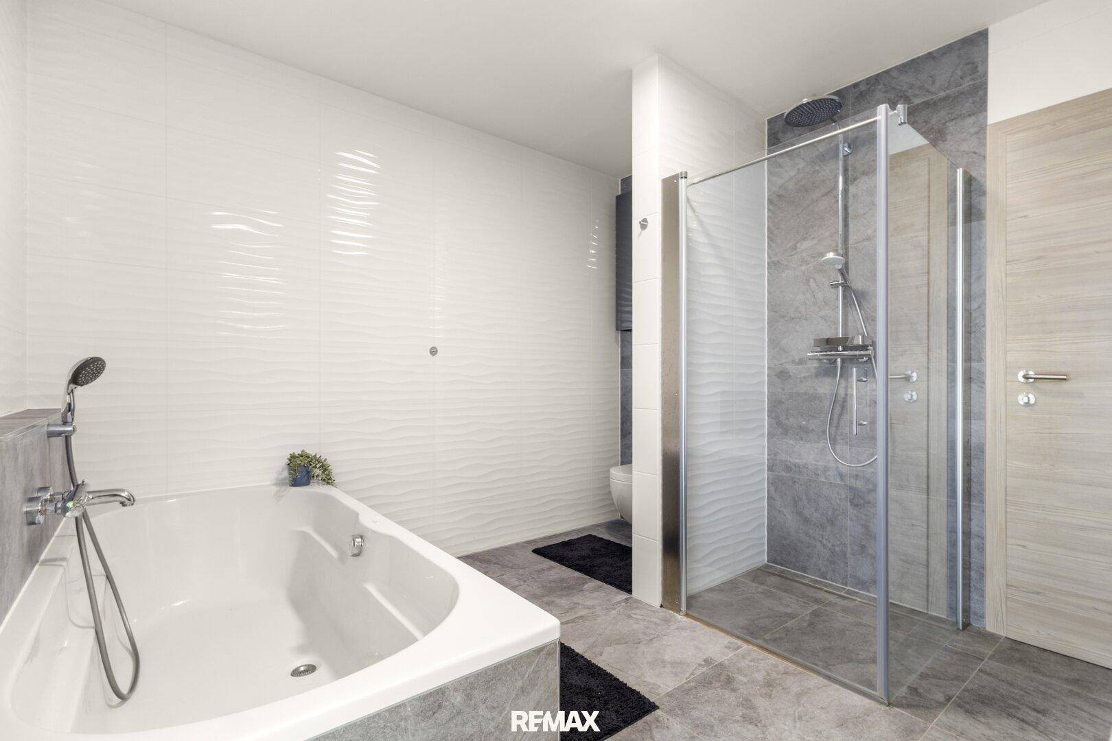 Modernes Badezimmer mit Badewanne, begehbarer Dusche und grauen Fliesen.