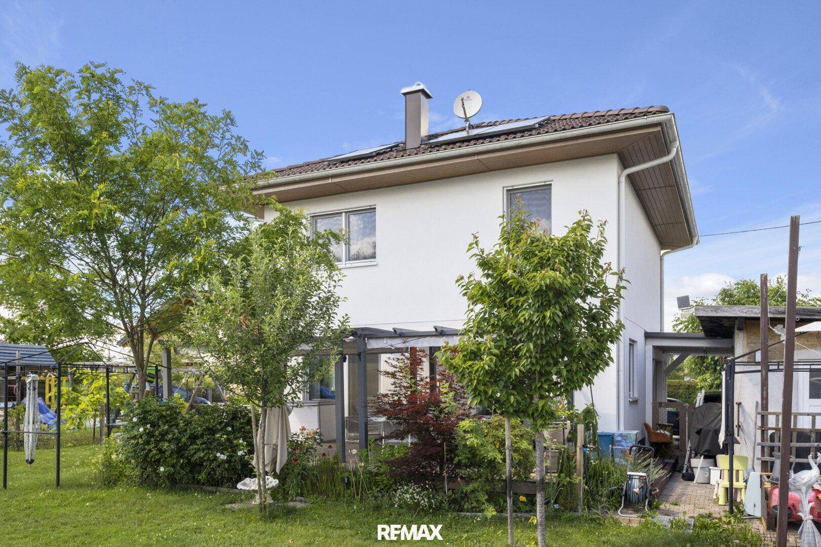 Gartenbereich mit üppiger Bepflanzung und einer überdachten Terrasse am Haus.
