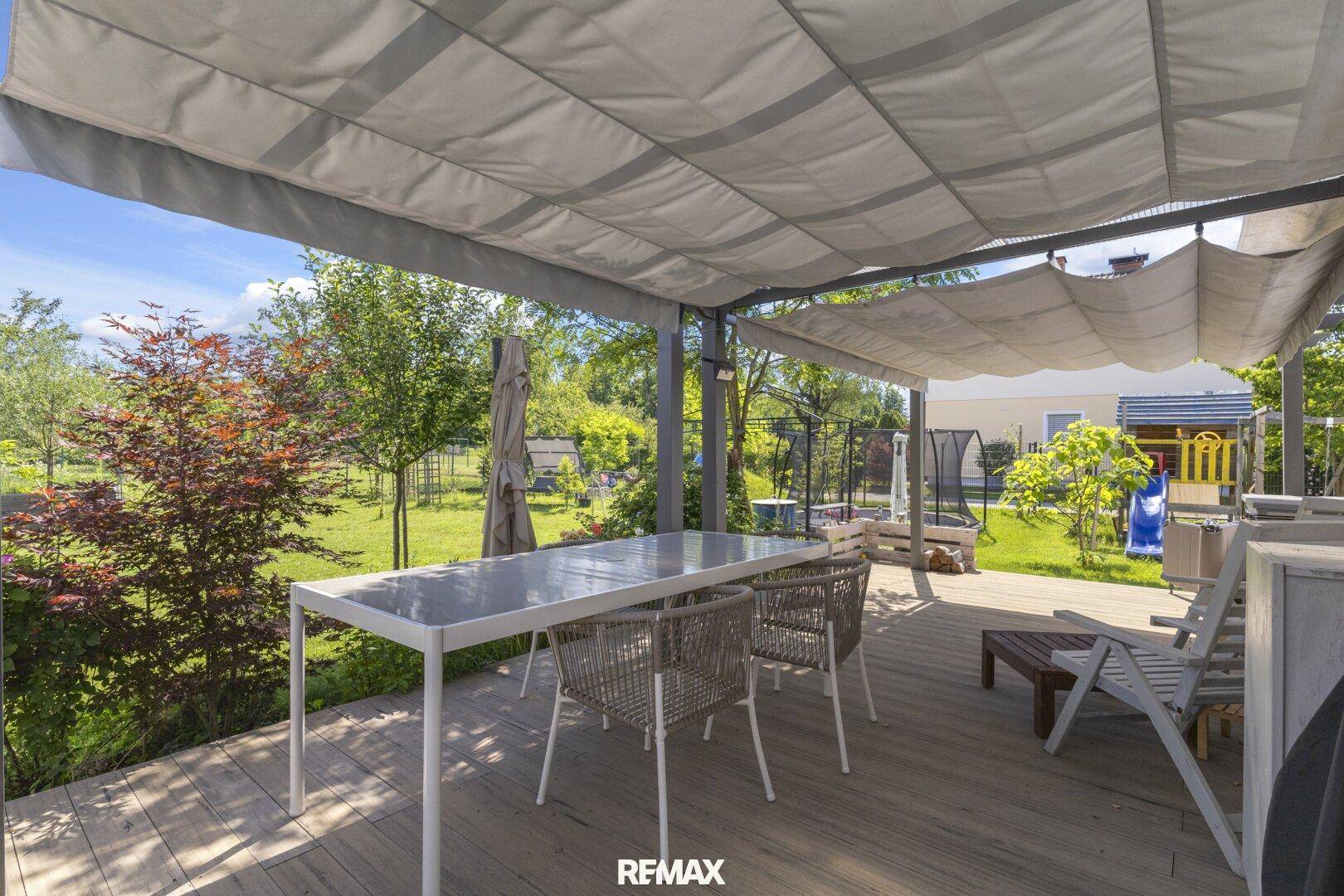 Überdachte Terrasse mit Esstisch und Stühlen, umgeben von einem grünen Garten.