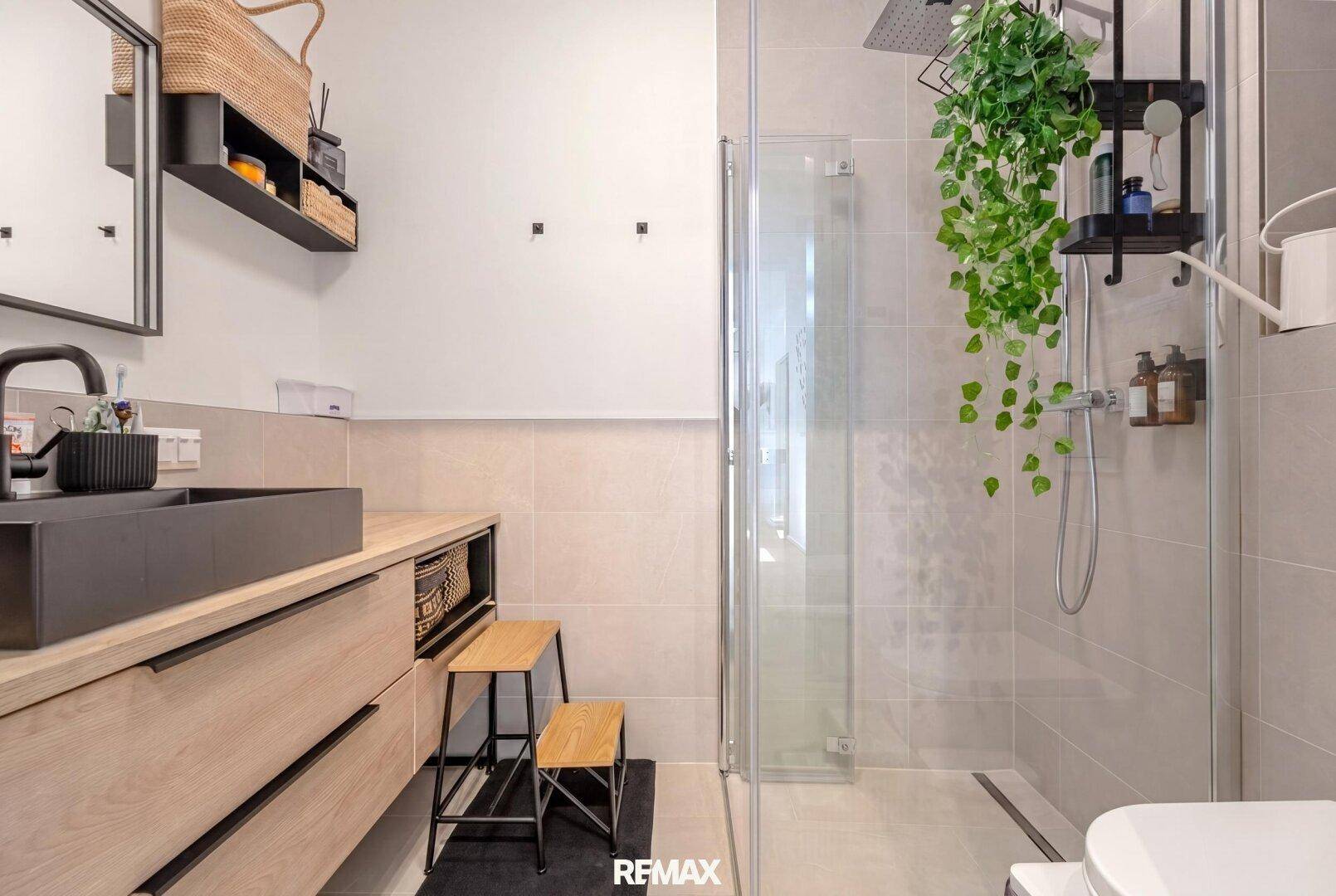 Modernes Badezimmer mit begehbarer Dusche, dunklem Waschbecken und hellen, großformatigen Fliesen.