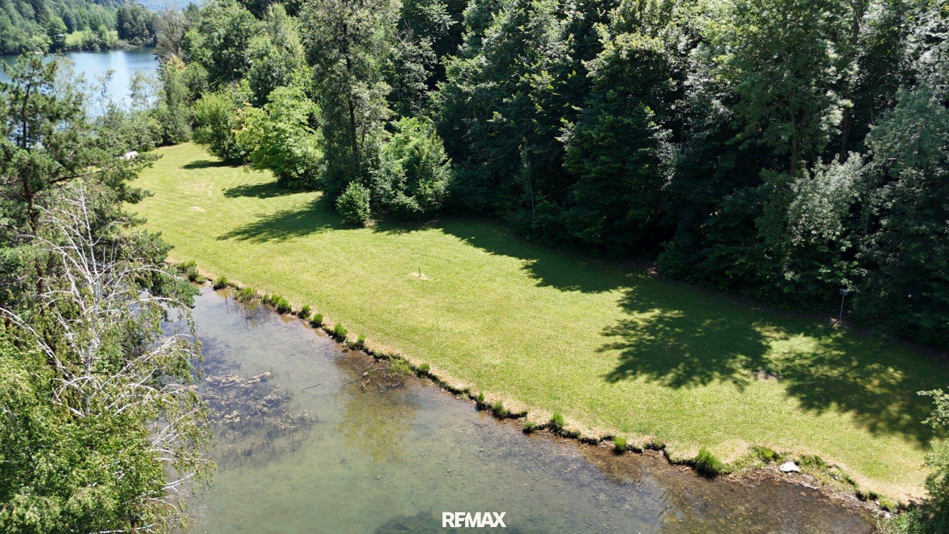 Luftaufnahme des Grundstücks mit Seezugang, umgeben von dichtem Wald und grünen Wiesen.