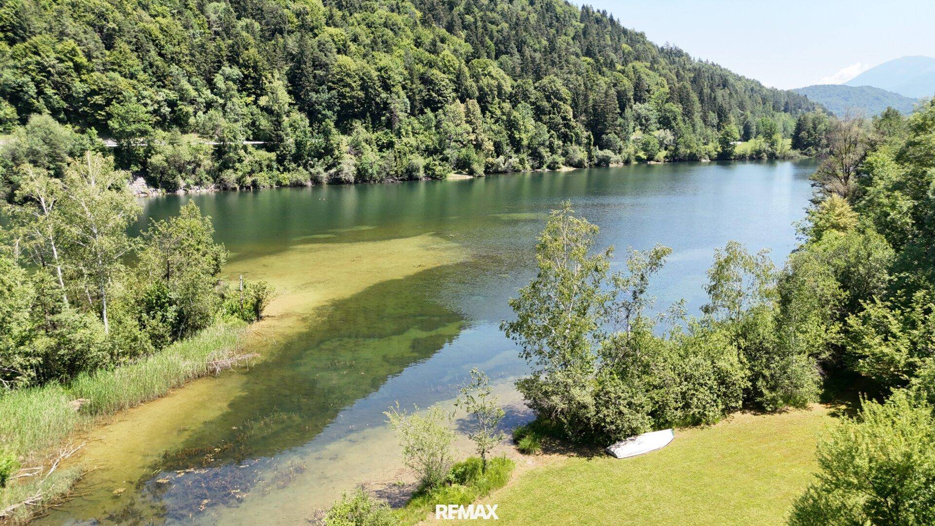 Luftaufnahme eines klaren Sees, umgeben von üppigem Grün und bewaldeten Hügeln.