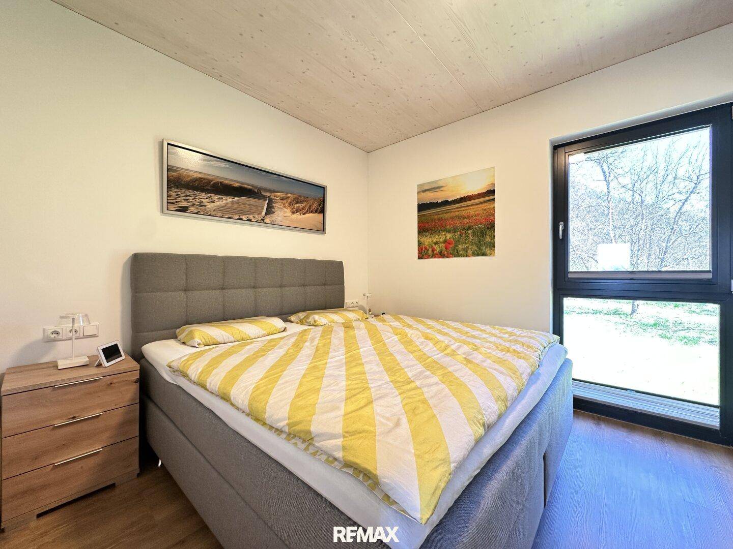 Gemütliches Schlafzimmer mit Doppelbett, Nachttisch und großem Fenster mit Blick ins Grüne.