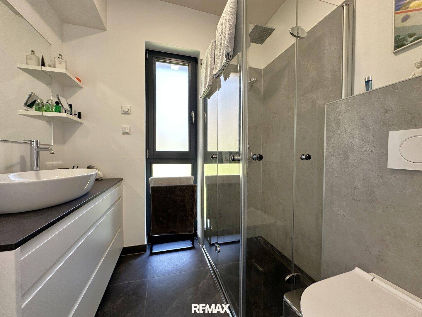 Modernes Badezimmer mit begehbarer Dusche, Waschtisch und Fenster für Tageslicht.