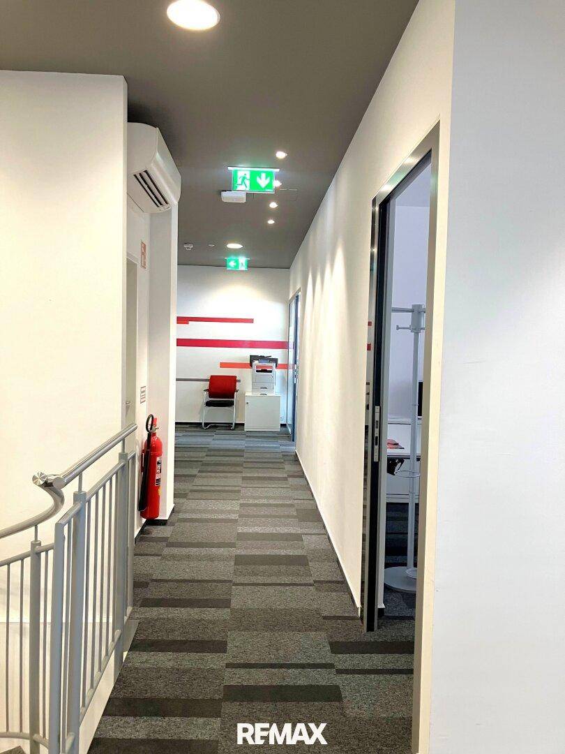 Langer Bürogang mit Teppichboden, Beleuchtung und Zugang zu verschiedenen Räumen.