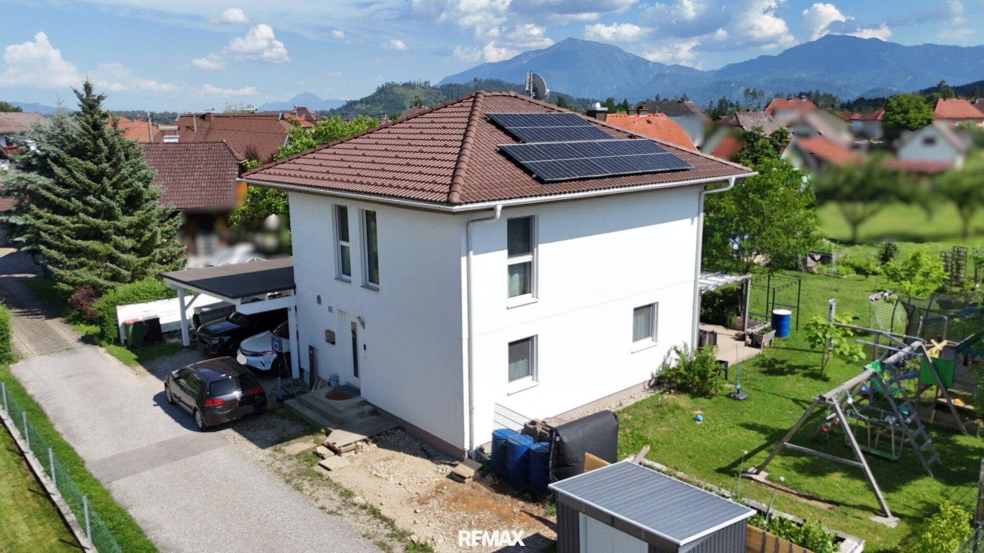 Seitenansicht des Einfamilienhauses mit Photovoltaikanlage auf dem Dach und Bergblick.