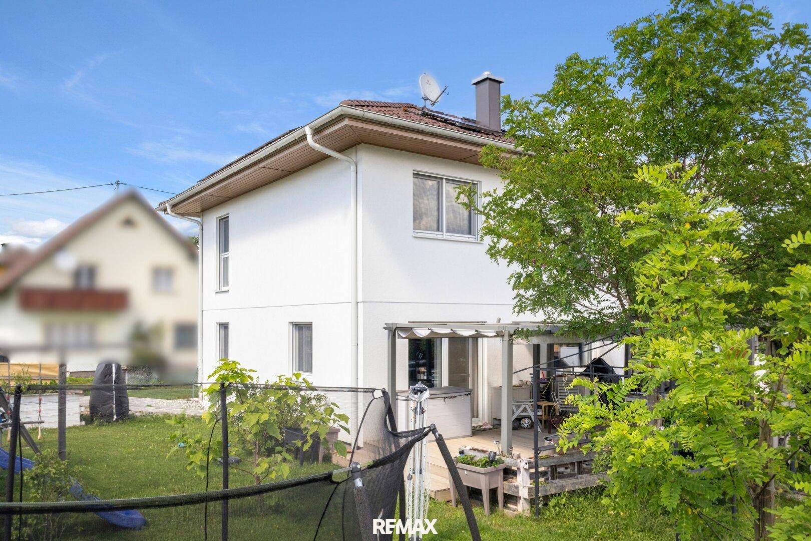 Rückansicht des Hauses mit überdachter Terrasse und Blick in den grünen Garten.