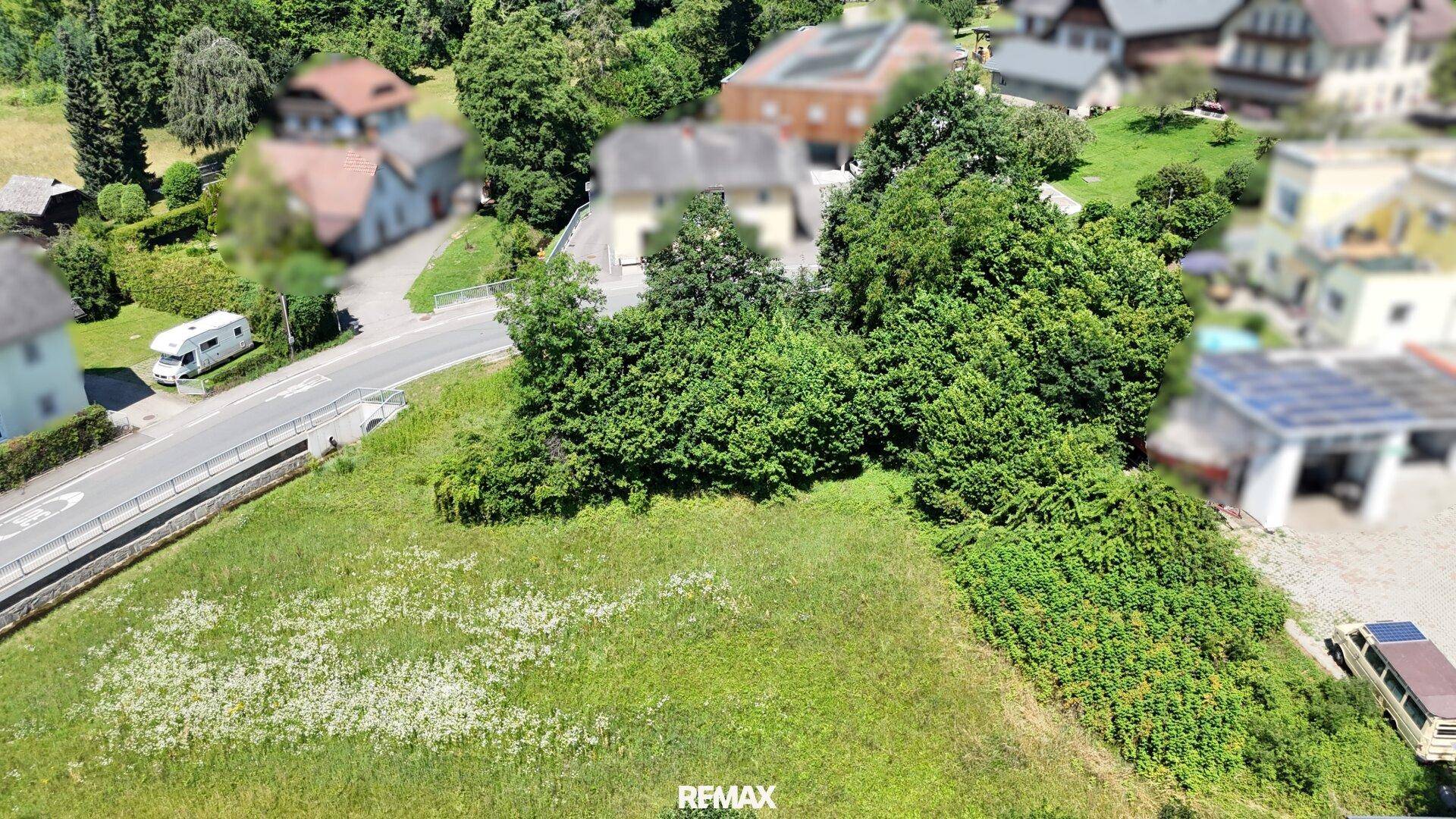 Panoramablick aus der Luft auf ein großes, grünes Grundstück neben einer Straße mit weiteren Häusern im Hintergrund.