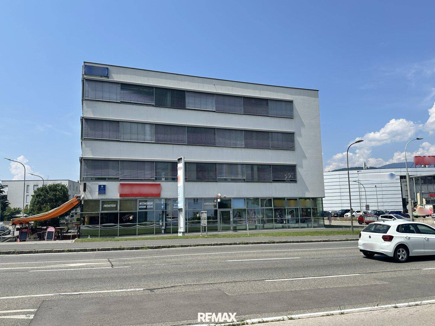 Ansicht des Geschäftsgebäudes von der Straße mit umliegenden Parkplätzen und klarem Himmel.
