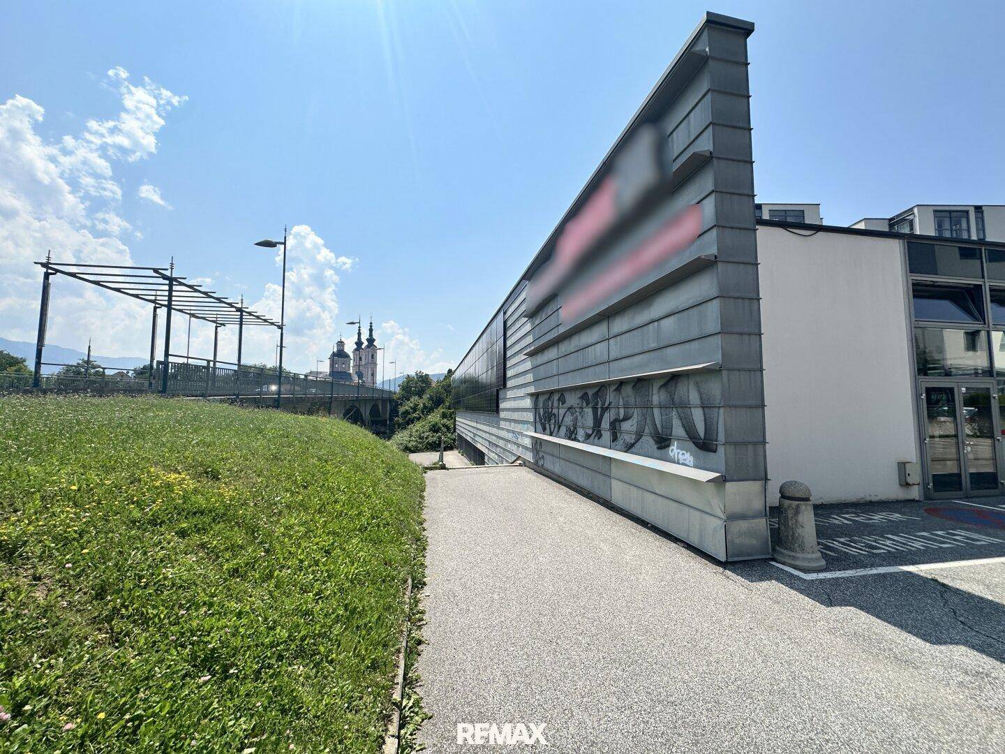 Seitliche Ansicht eines Gebäudes mit moderner Fassade und Grünfläche unter blauem Himmel.