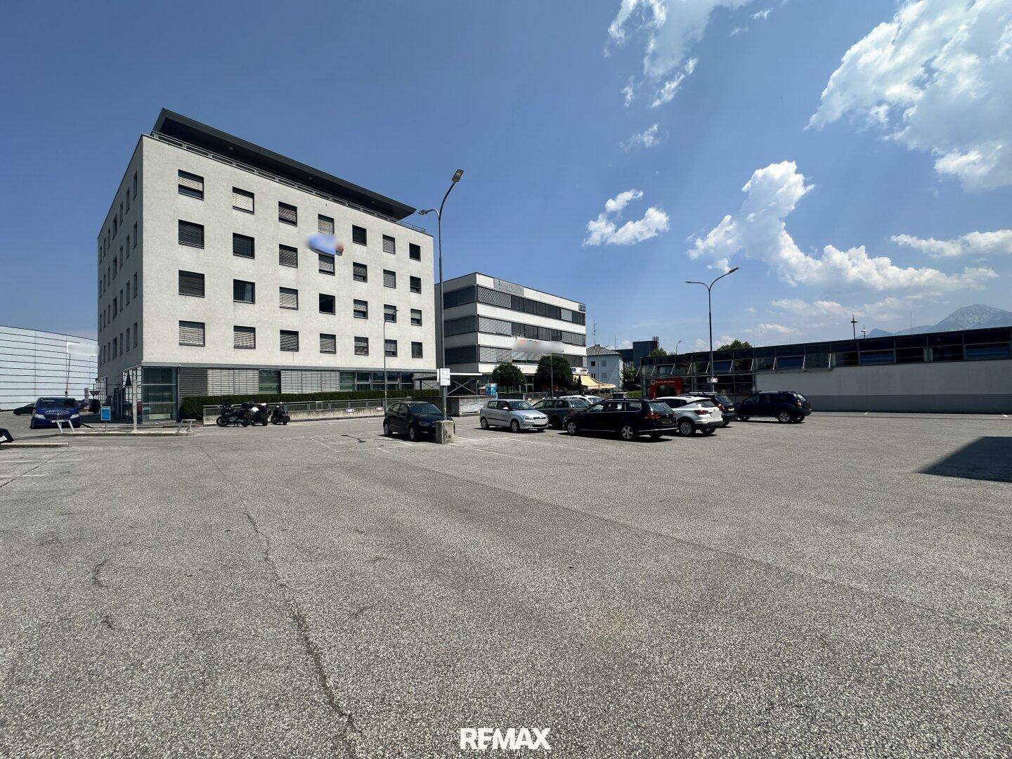 Großer asphaltierter Parkplatz vor modernen Geschäftsgebäuden unter blauem Himmel.