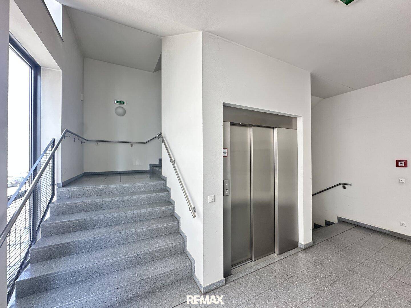 Heller Treppenaufgang mit Aufzug und Handläufen in einem modernen Gebäude.