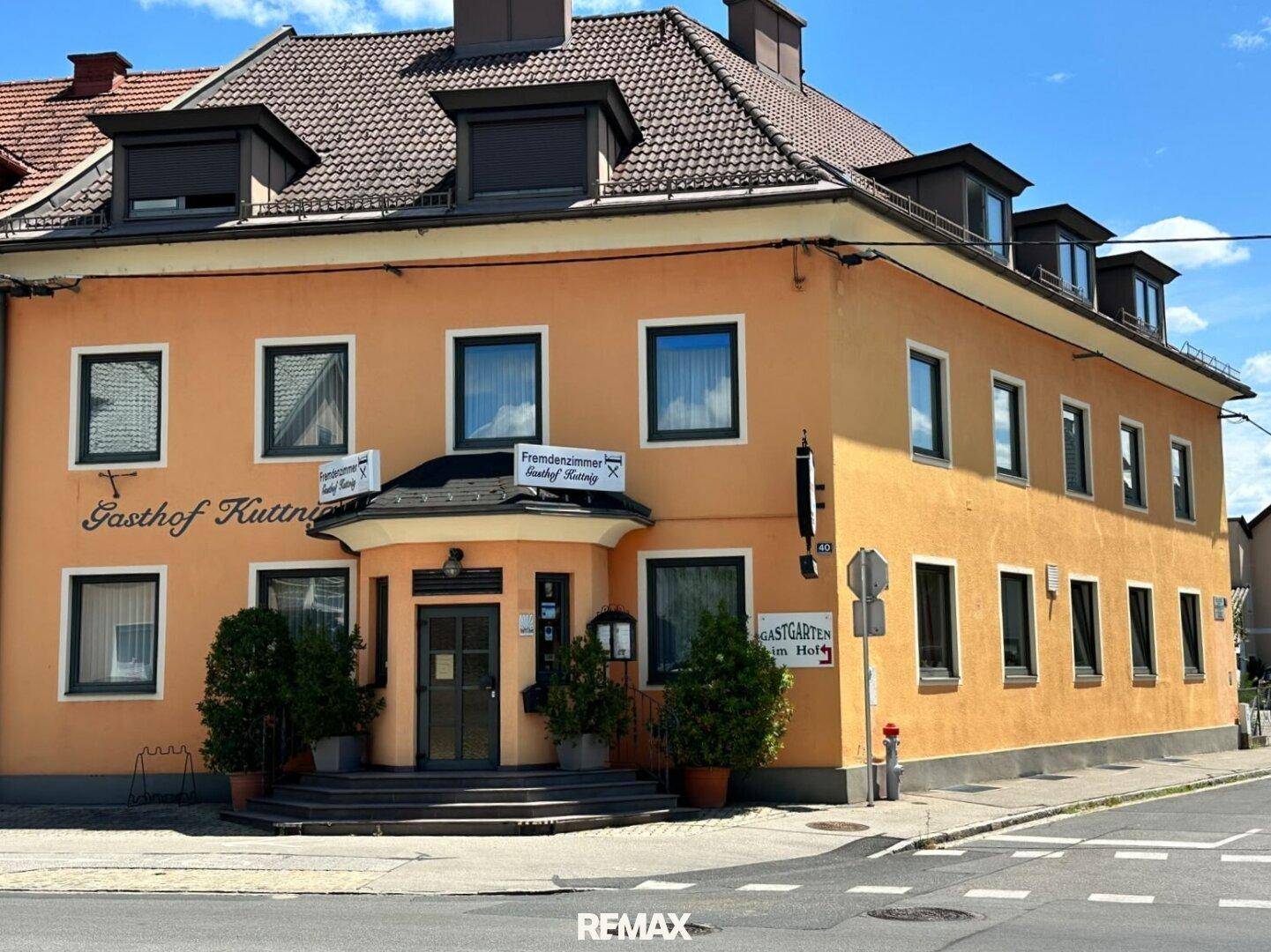 Nahaufnahme des Gasthofs mit orangefarbener Fassade, Dachgauben und Beschilderung an der Straßenecke.